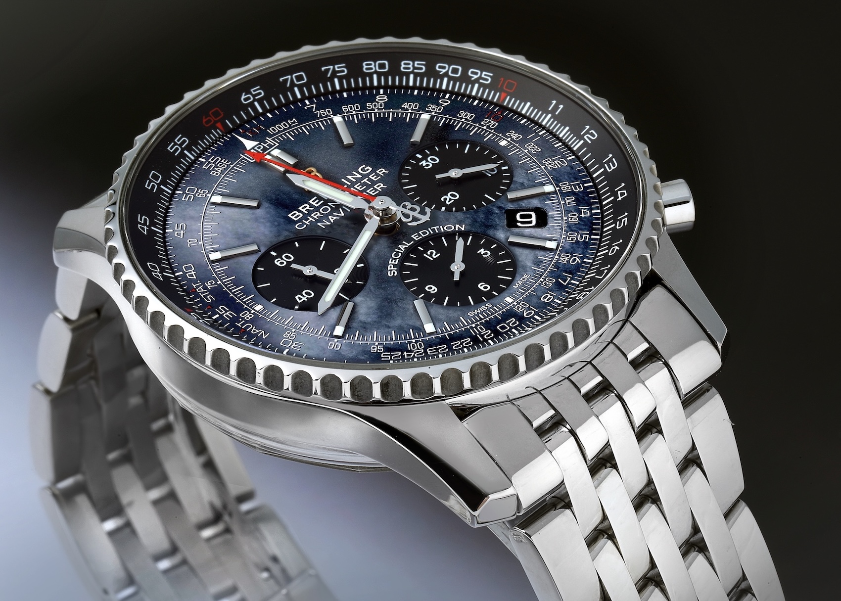 A close-up, angled shot of a Breitling Navitimer 01 watch featuring a stunning blue mother-of-pearl dial with black subdials, a steel case, and a multi-link steel bracelet.