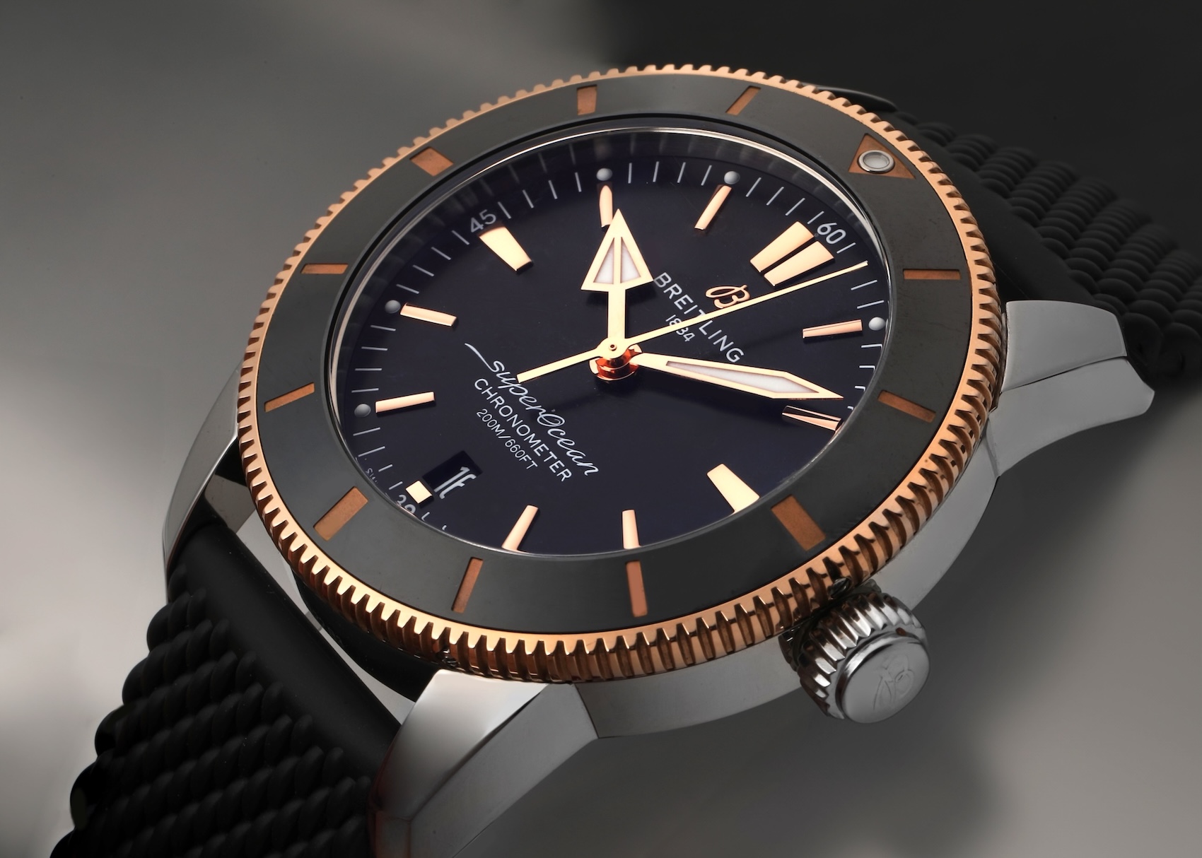 A sophisticated Breitling Superocean Heritage II dive watch with a two-tone steel case and 18k rose gold bezel, a black dial with gold accents, and a black textured rubber strap.