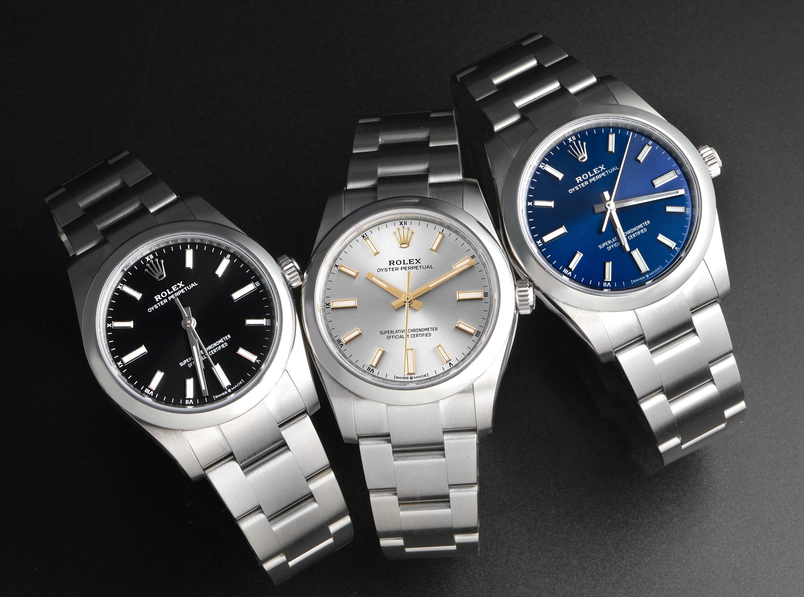 Three stainless steel Rolex Oyster Perpetual 34mm watches shown side-by-side with black, silver, and blue dials.