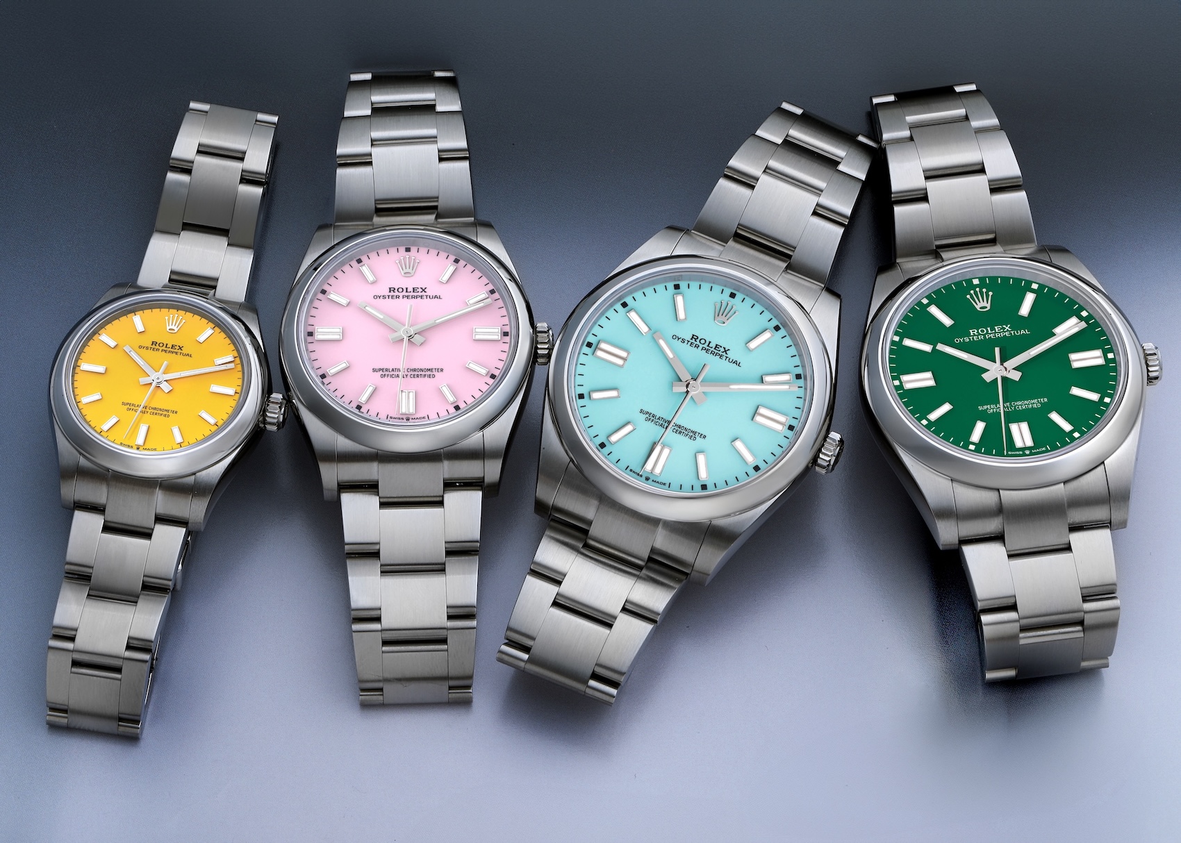 A lineup of four Rolex Oyster Perpetual watches, showcasing the colorful lacquer dials in yellow, candy pink, turquoise, and green.