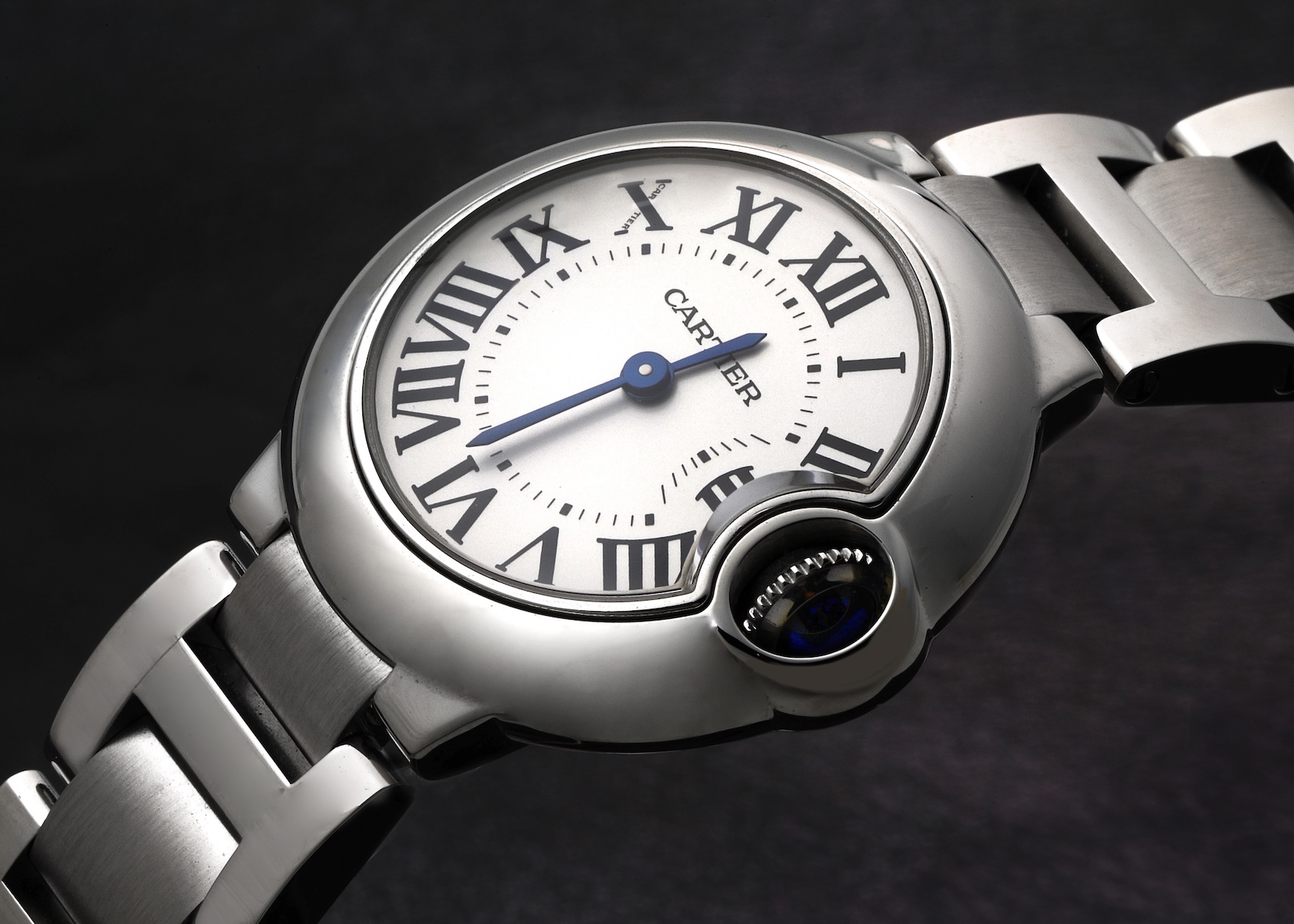 An angled studio shot of a Cartier Ballon Bleu midsize steel watch, featuring its signature white dial with black Roman numerals, blued-steel hands, and the iconic blue cabochon crown.