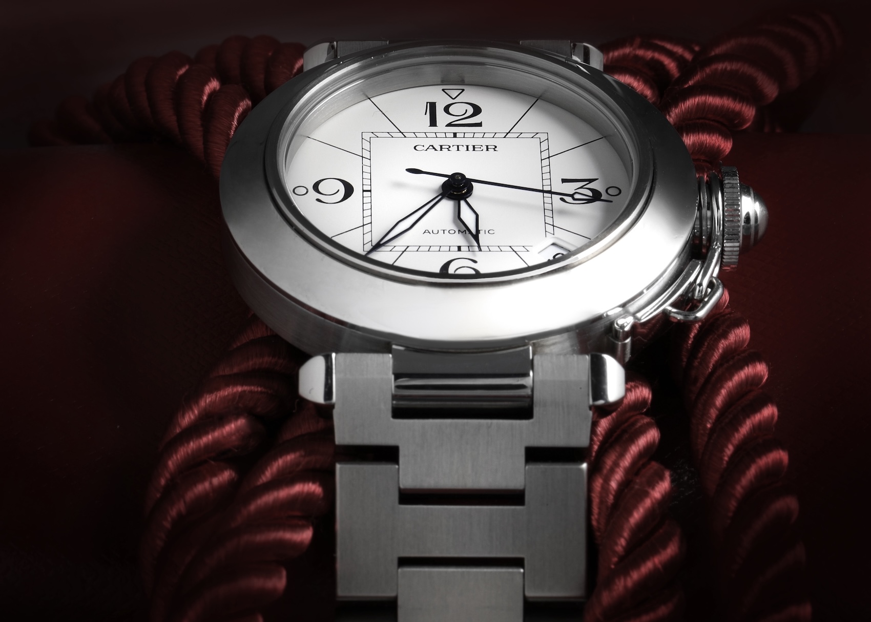 A Cartier Pasha C midsize watch in stainless steel, posed on a red rope. The watch has a clean white dial featuring the signature 12, 3, 6, and 9 Arabic numerals and a date window.