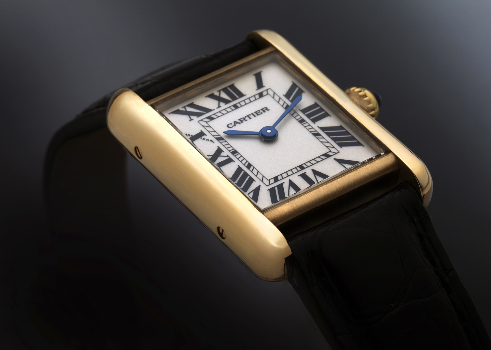 A close-up, angled view of the iconic Cartier Tank Louis watch, highlighting its 18k yellow gold rectangular case, classic white dial with black Roman numerals, blued-steel hands, and black alligator strap.