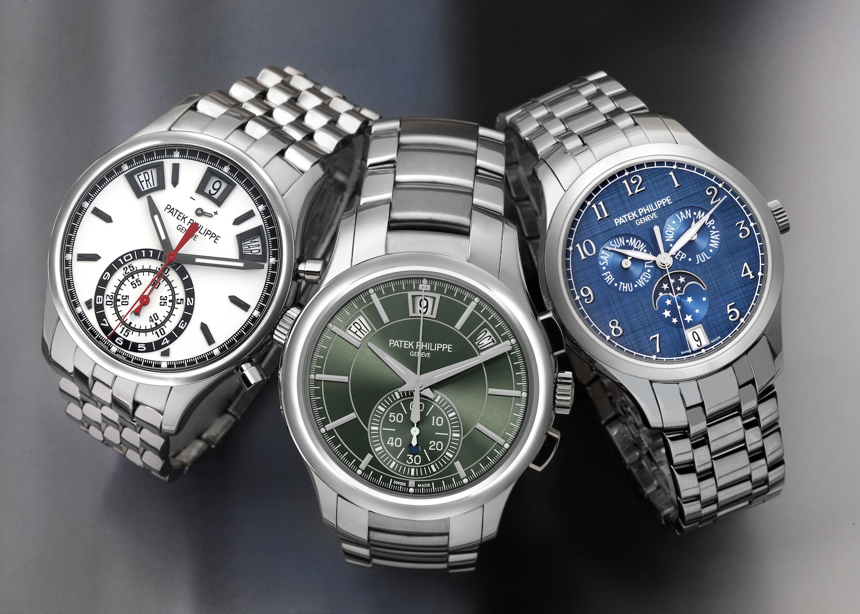 A group of three Patek Philippe Annual Calendar watches in stainless steel. The models shown include a white dial chronograph, a green dial chronograph, and a blue dial with a moonphase display, all on steel bracelets.