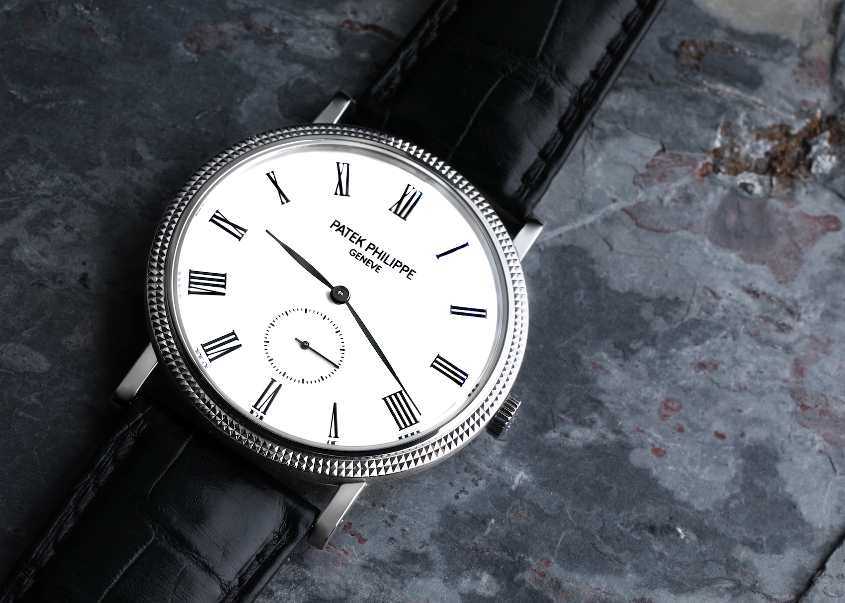 A Patek Philippe Calatrava ref 5119G in white gold, featuring a white dial with black Roman numerals, a small seconds sub-dial, and the iconic "Clous de Paris" hobnail bezel, paired with a black alligator strap.