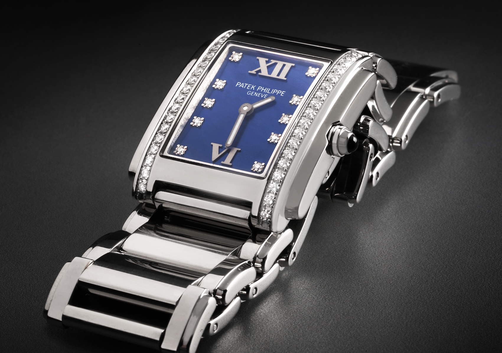 A close-up of a Patek Philippe Twenty-4 steel ladies' watch (4910A) with a deep blue dial, diamond hour markers, and a rectangular case set with two rows of brilliant-cut diamonds.