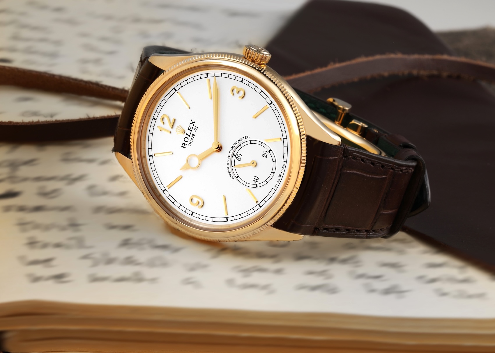 The elegant Rolex 1908 watch in 18k yellow gold with a white dial and brown leather strap, resting on the pages of a handwritten journal to emphasize its classic style.
