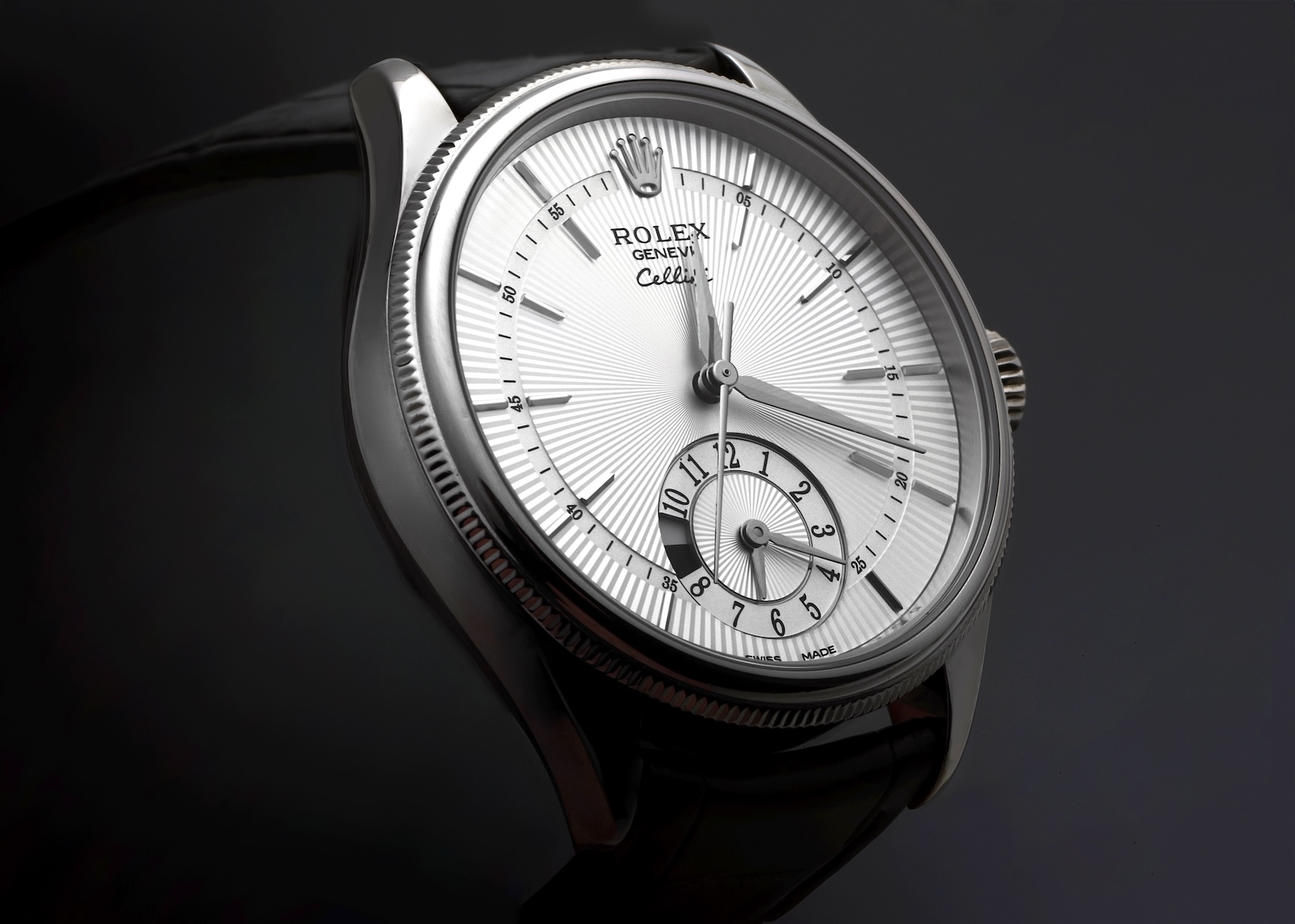 An angled macro shot of a Rolex Cellini Dual Time watch in 18k white gold, highlighting the silver guilloché dial and the dual-time subdial, on a black leather strap.