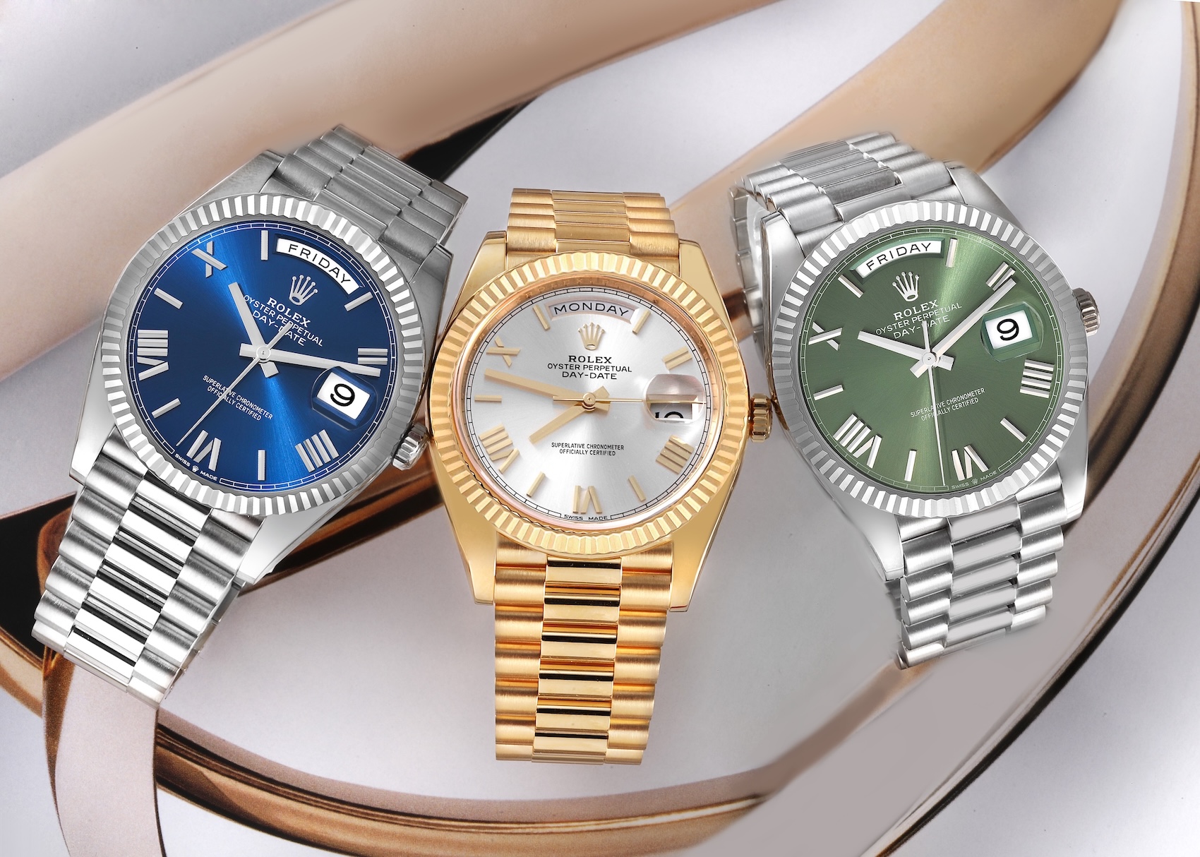 A trio of Rolex Day-Date 40 watches in platinum, yellow gold, and white gold, showcasing blue, silver, and olive green dials with Roman numerals.