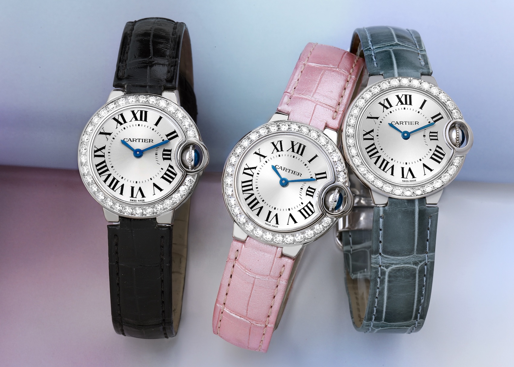 Three Cartier Ballon Bleu 28mm small model watches with diamond bezels on black, pink, and grey leather straps.