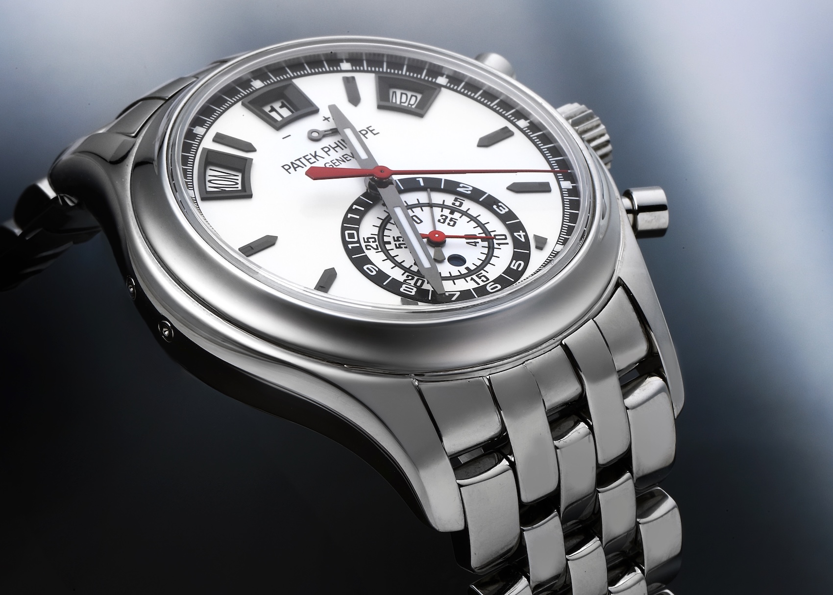 Close-up of the Patek Philippe Ref. 5960/1A-001 in stainless steel. The image details the white opaline dial, red chronograph hands, three calendar apertures for Day, Date, and Month at the top, and the signature 5-row "droplet" link steel bracelet.