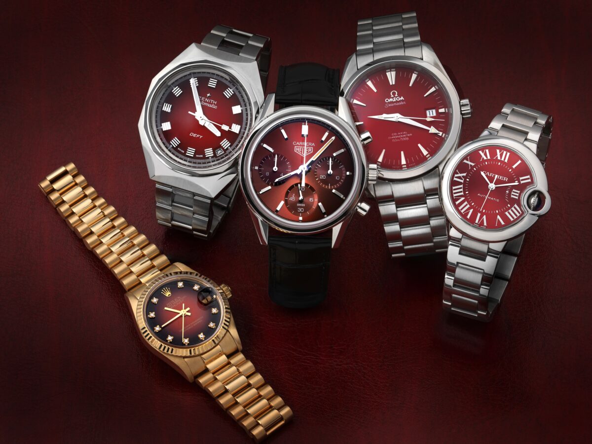 Collection of luxury watches with deep red dials including a gold Rolex Datejust, Zenith Defy Revival, TAG Heuer Carrera, Omega Aqua Terra, and Cartier Ballon Bleu, illustrating the Divine Damson color trend.