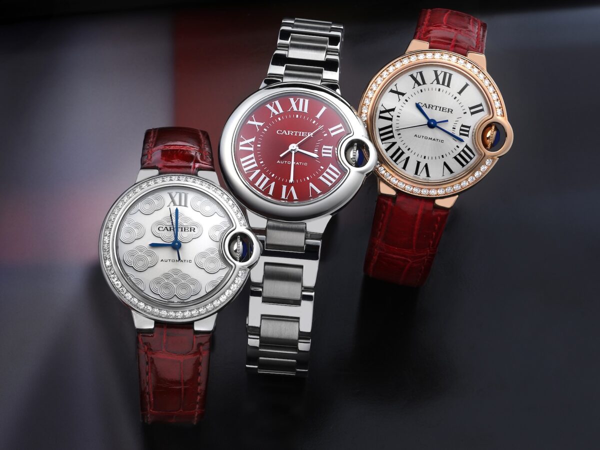 A trio of Cartier Ballon Bleu ladies' watches featuring a steel model with a red dial, a rose gold model with a diamond bezel, and a limited edition silver dial model, all arranged on a dark background.