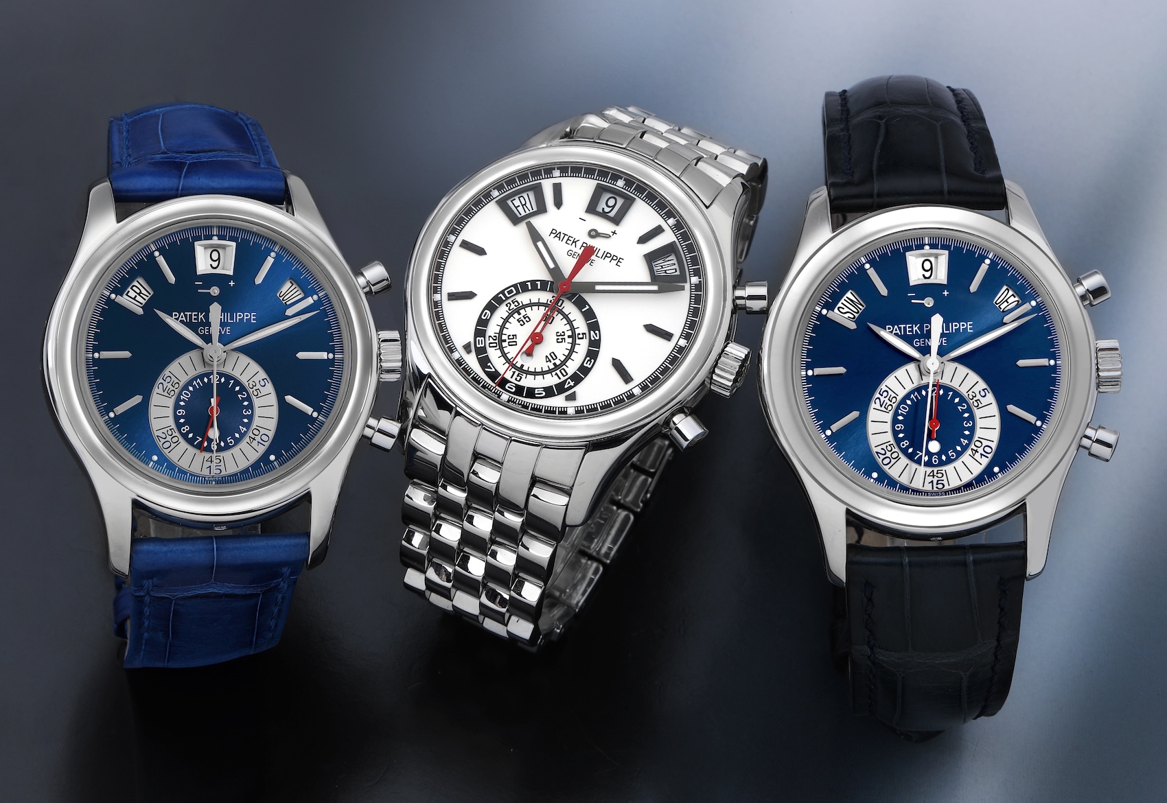 Three Patek Philippe Annual Calendar Chronograph Ref. 5960 watches arranged together. The center watch is the stainless steel Ref. 5960/1A with a white dial and steel bracelet, flanked by two platinum Ref. 5960P models with blue dials and blue alligator leather straps.