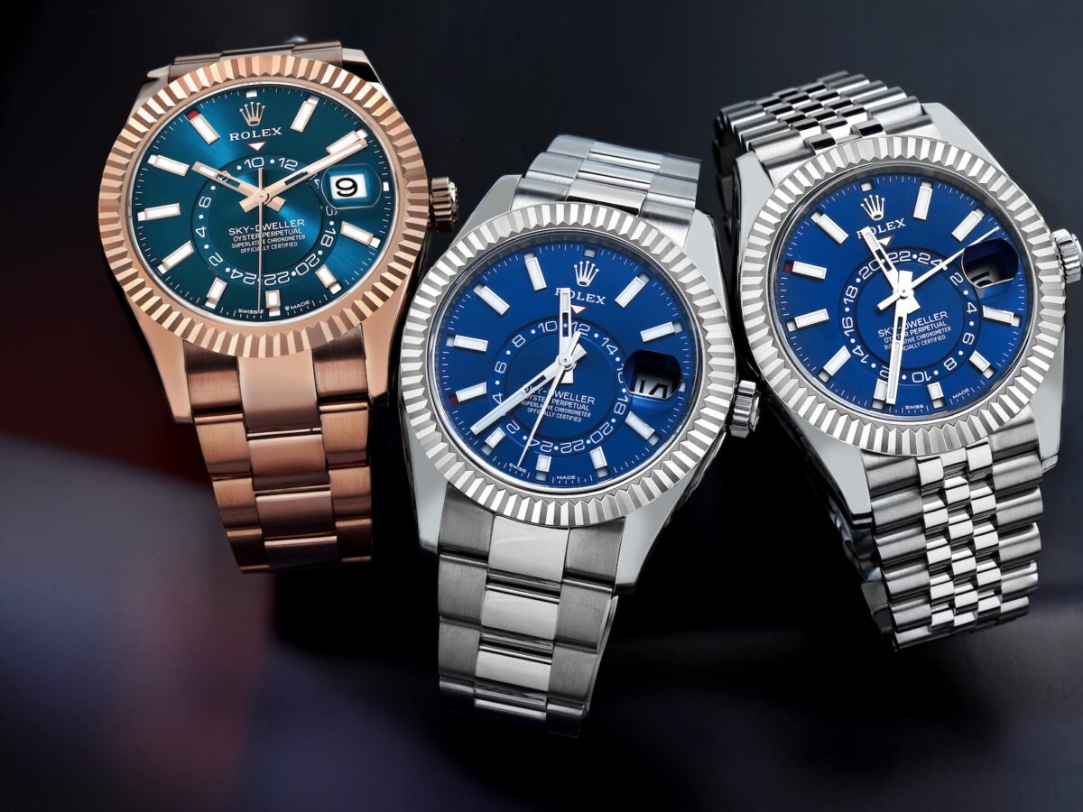 A group shot of three Rolex Sky-Dweller watches—one in Everose gold and two in Oystersteel—resting on a dark surface, showcasing the various bracelet and metal combinations.