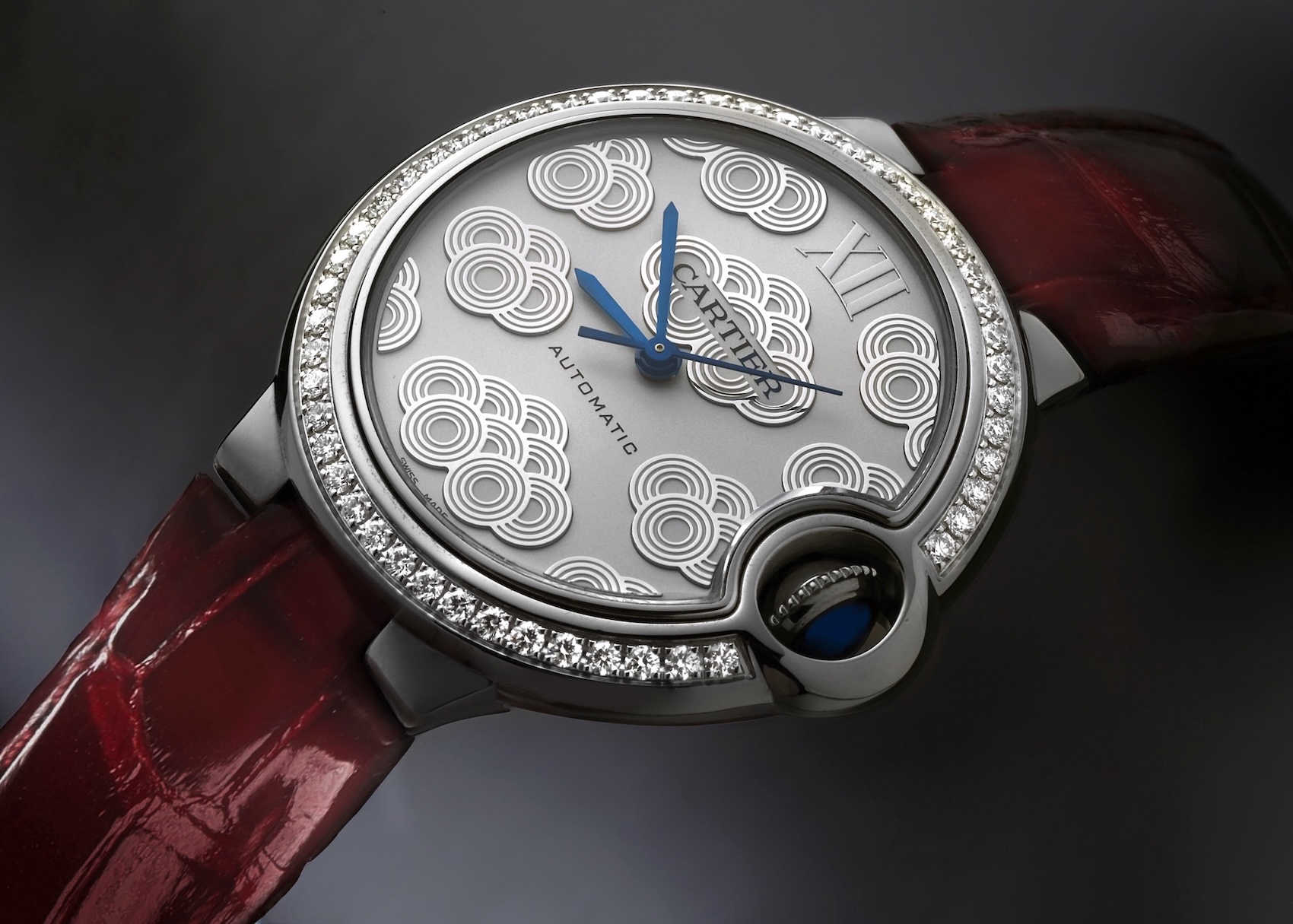 A 33mm Cartier Ballon Bleu ladies' watch featuring a diamond-set bezel, a silver dial with a geometric "Lucky Clouds" pattern, and a deep red alligator leather strap.