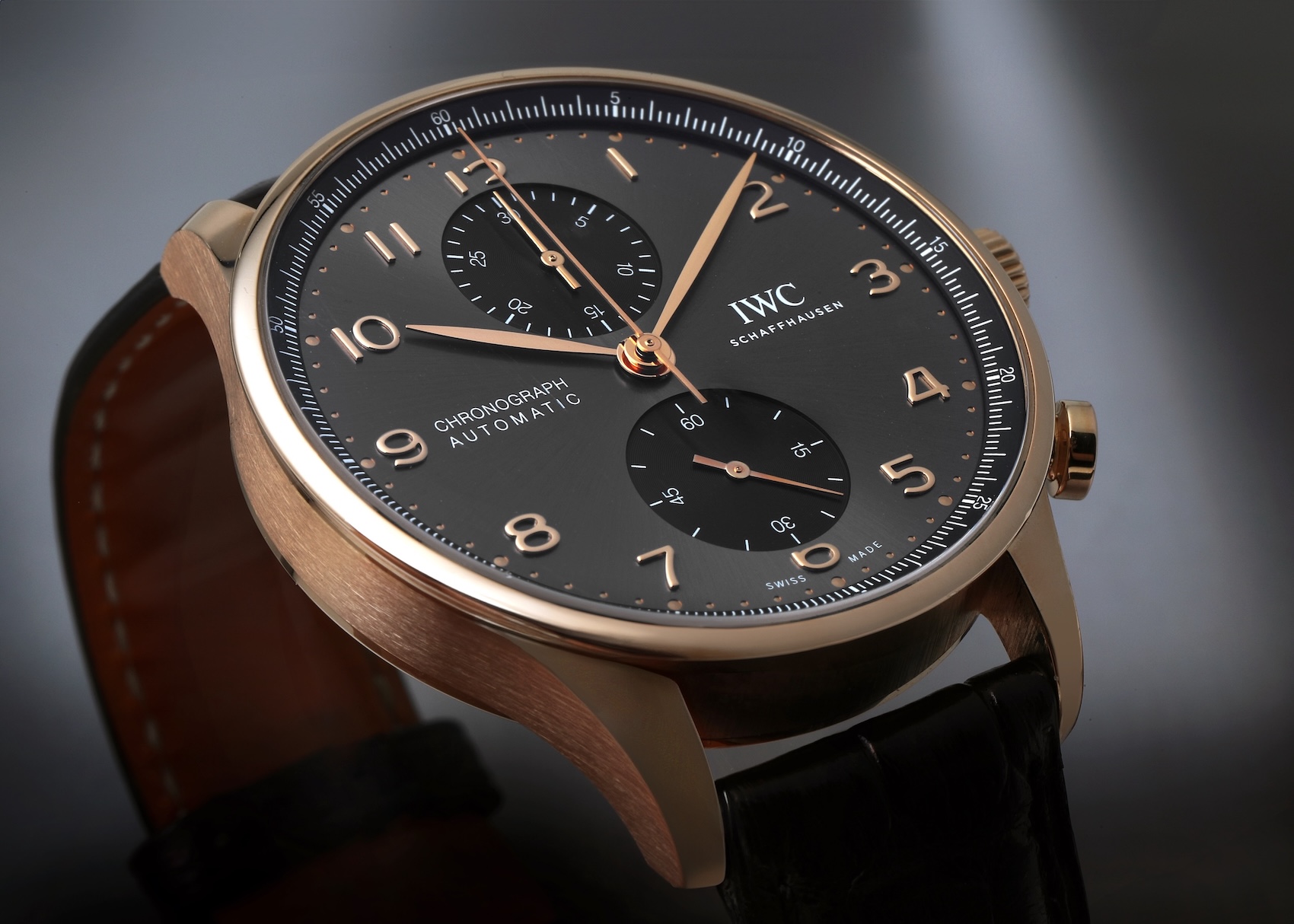 An IWC Portugieser Chronograph in an 18k rose gold case with a slate-colored dial, gold Arabic numerals, and a black alligator leather strap.