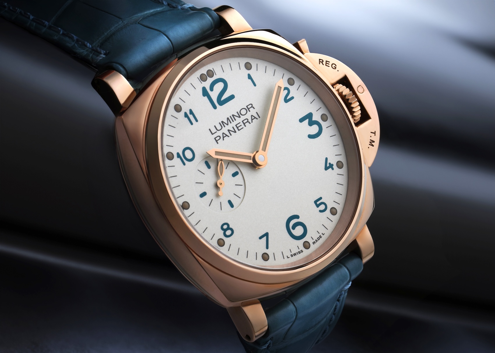 An angled view of a Panerai Luminor Due in rose gold with an ivory dial and blue Arabic numerals, fitted on a dark blue alligator leather strap.