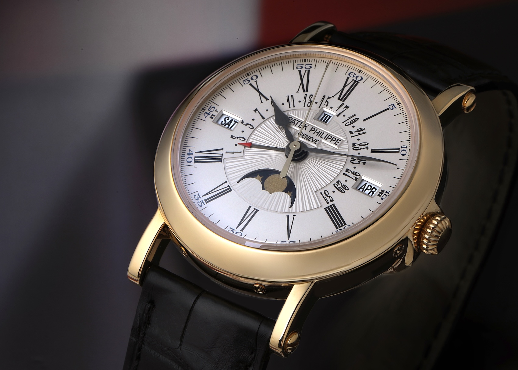 Angled view of a Patek Philippe Perpetual Calendar 5159J in 18k yellow gold featuring a silver opaline dial, Roman numerals, and a black leather strap.