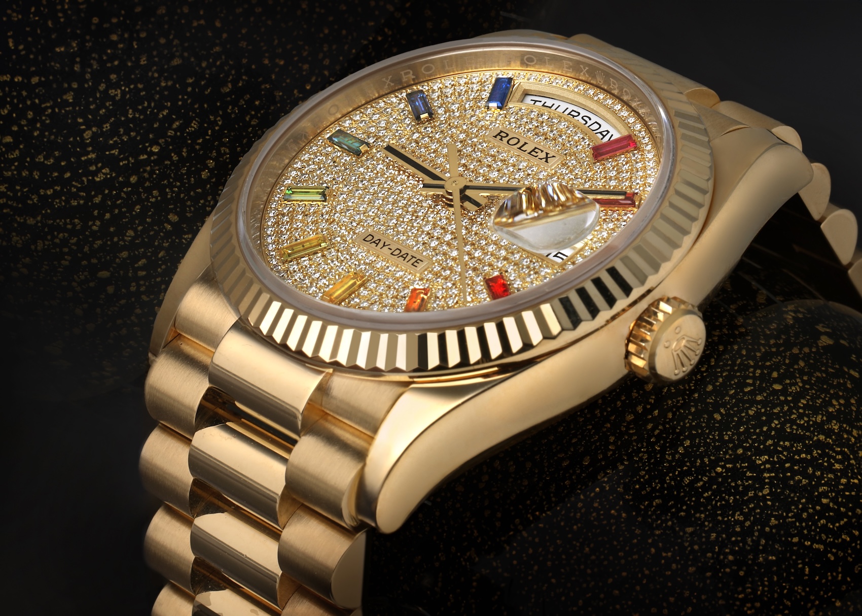 An angled view of the Rolex 128238 showing the full President bracelet, the diamond-paved dial, and the vibrant baguette-cut rainbow sapphires under studio lighting.