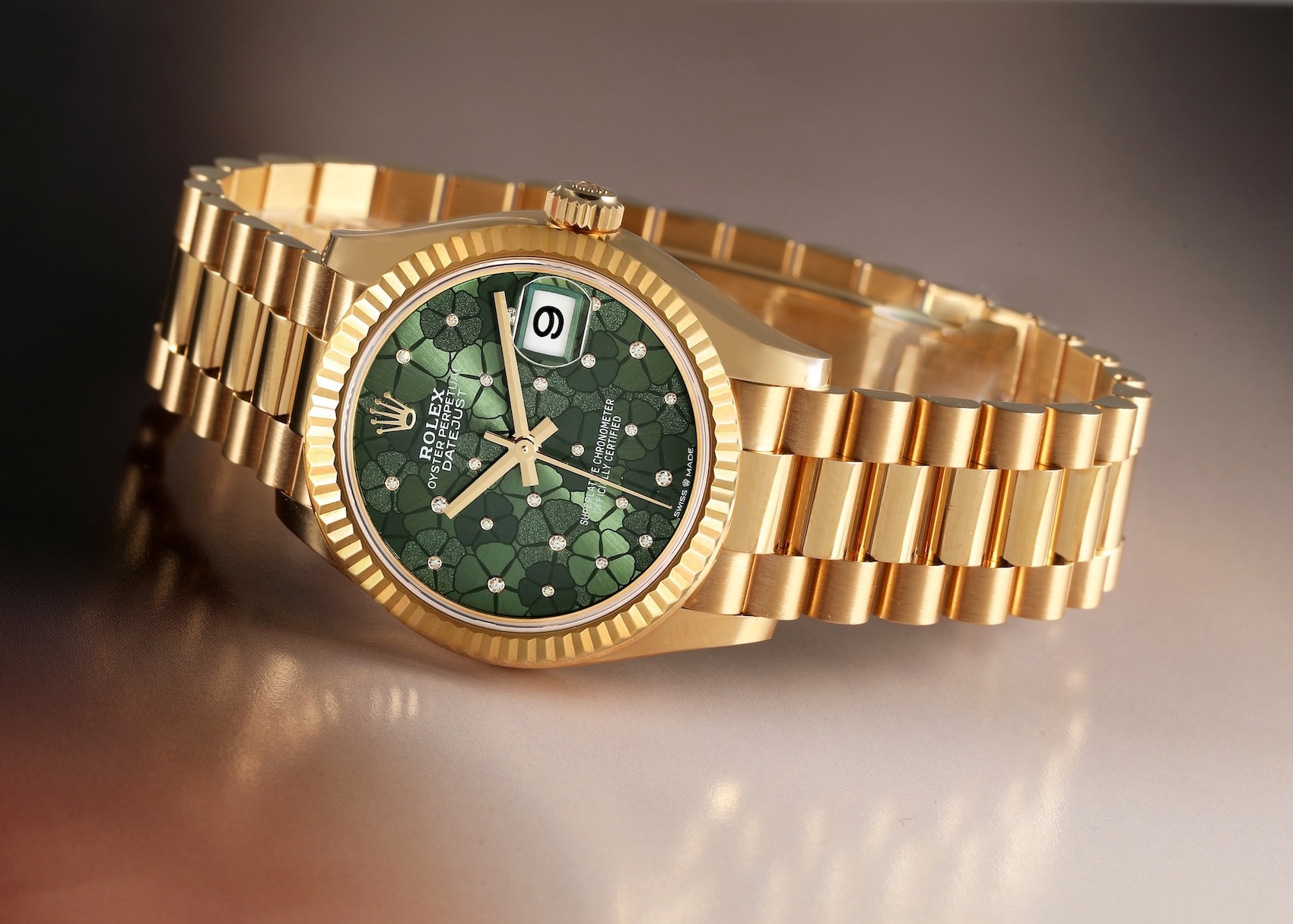 A 31mm 18k yellow gold Rolex Datejust with a President bracelet and a textured olive green dial decorated with a floral motif and tiny diamonds.