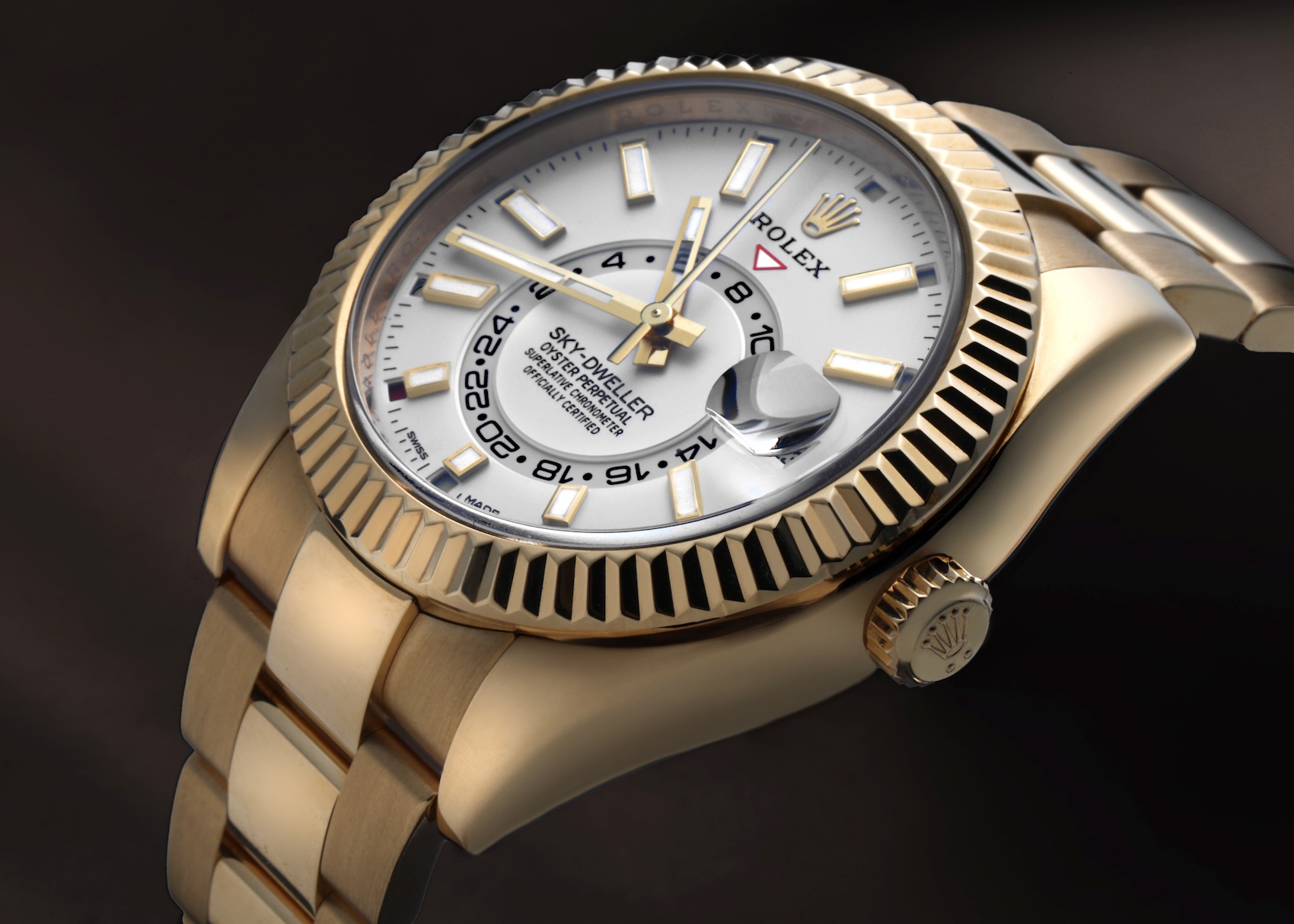 A side-profile view of a solid 18k yellow gold Rolex Sky-Dweller with a crisp white dial and signature fluted bezel on an Oyster bracelet.