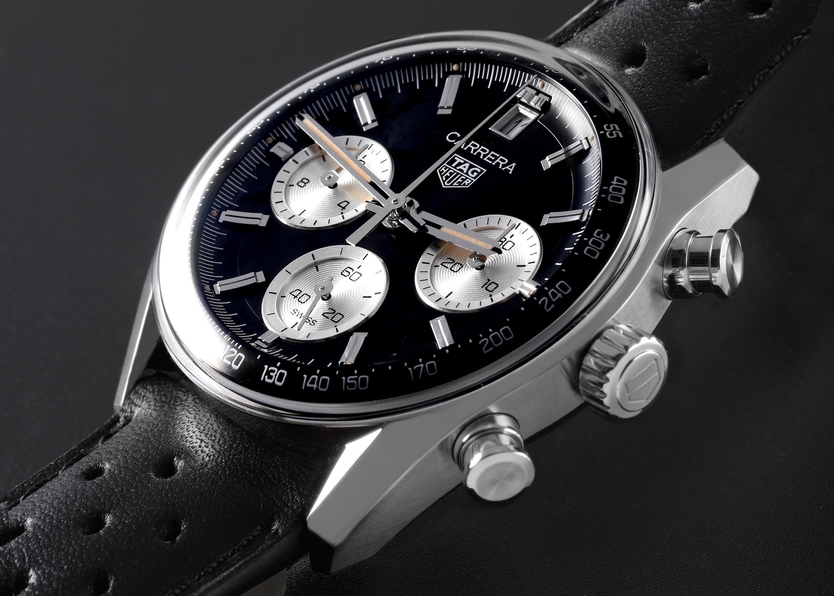 A close-up side profile of a TAG Heuer Carrera Chronograph with a "Reverse Panda" black and silver dial and a domed sapphire crystal.