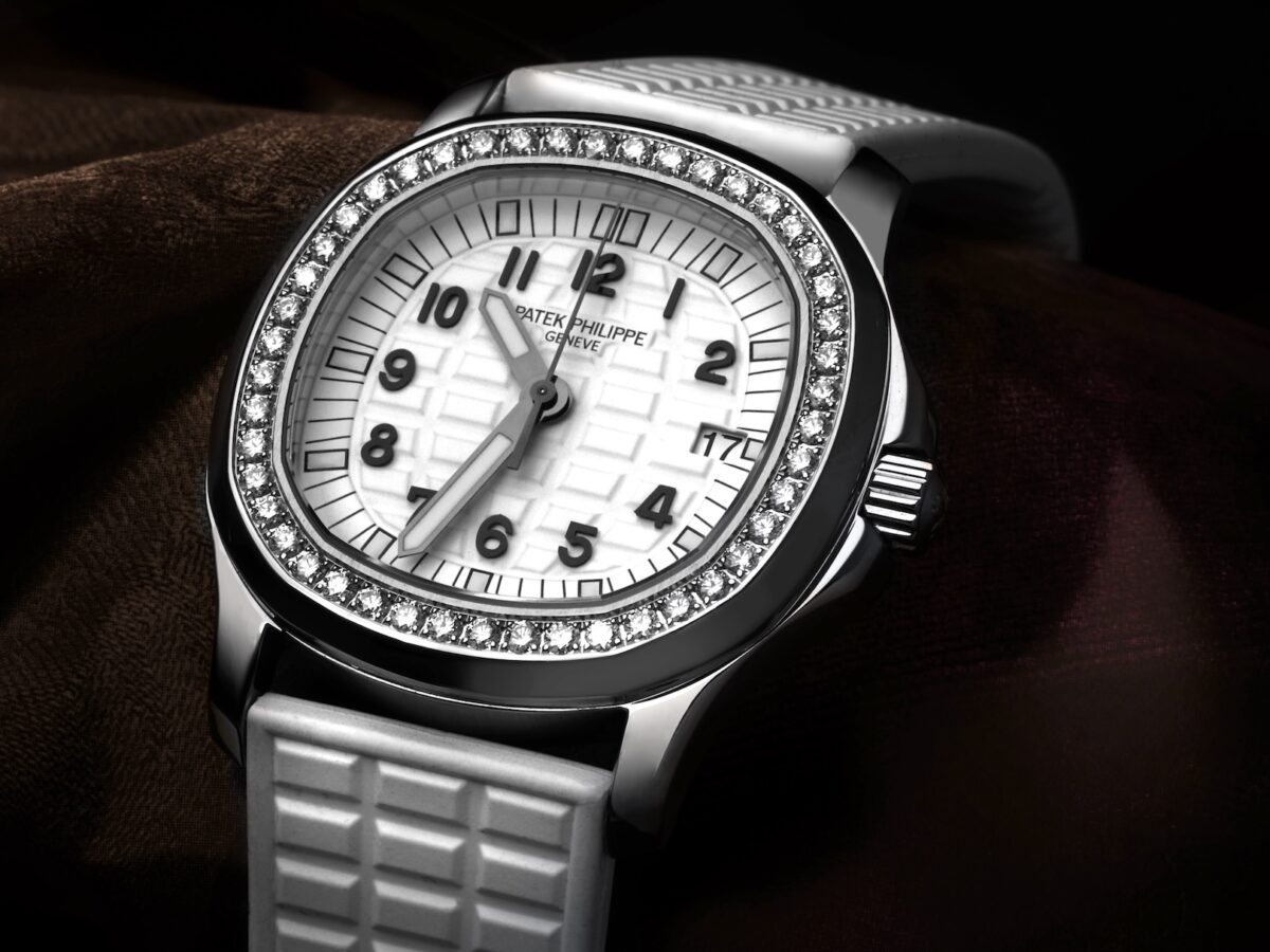 A close-up, high-angle shot of a Patek Philippe Aquanaut Luce 5067A ladies' watch resting on a textured dark fabric. The watch features a stainless steel case, a bezel set with brilliant-cut diamonds, a white embossed dial with black Arabic numerals, and a matching white "Tropical" rubber strap.
