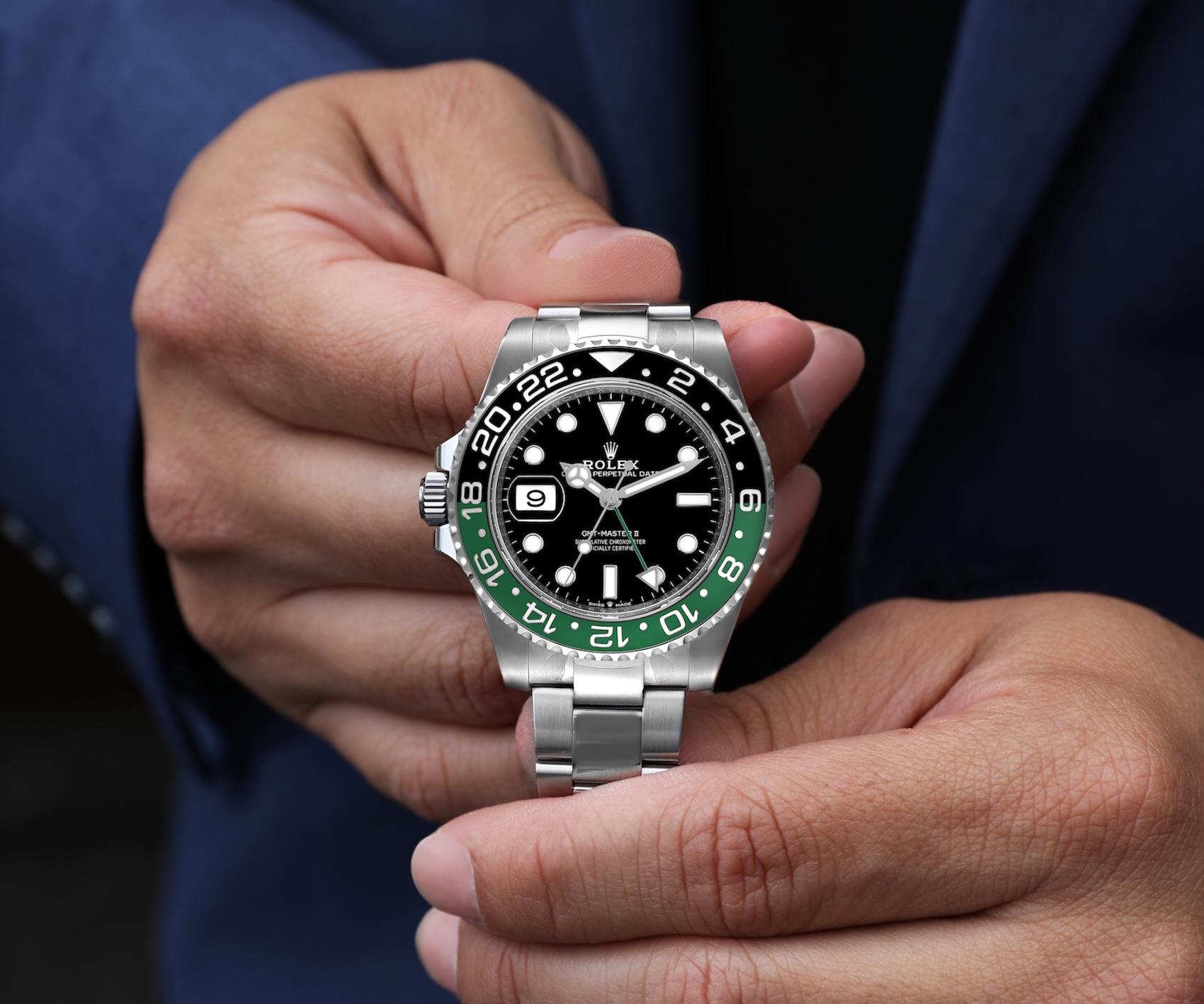 Two hands holding a Rolex GMT-Master II Sprite in stainless steel, showcasing the black dial and green and black ceramic bezel.