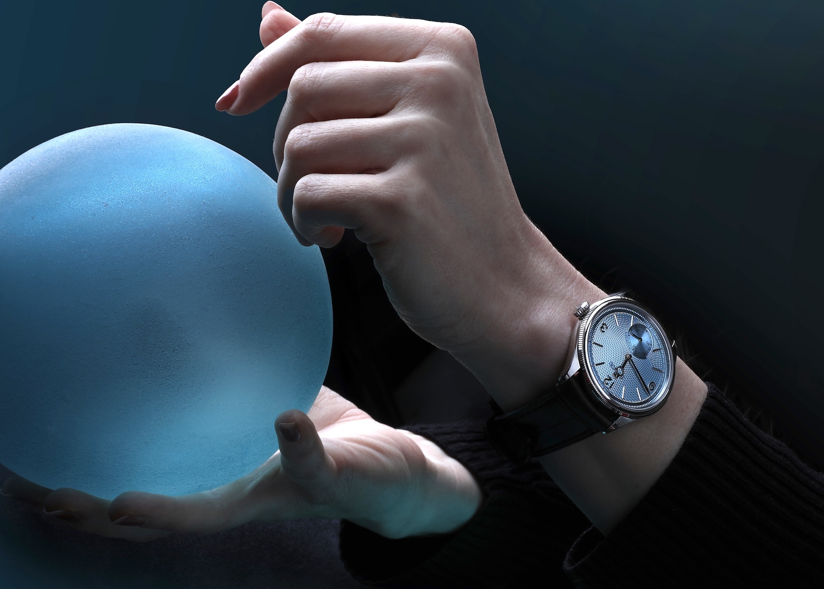 A moody, artistic photograph of a model holding a glowing blue frosted sphere, wearing the Rolex 1908 in platinum with an ice-blue dial on a brown leather strap.