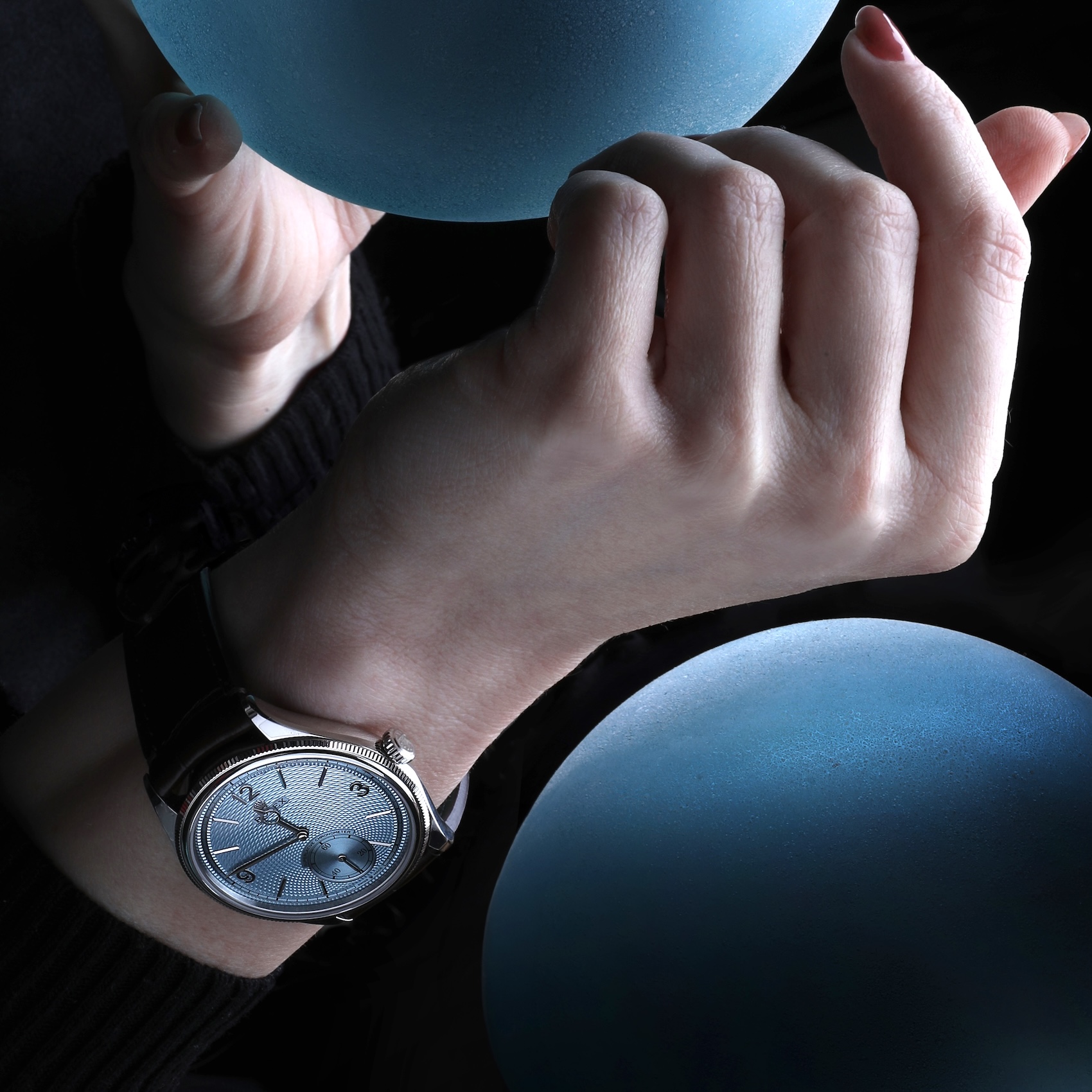  A stylish wrist shot of the Rolex 1908 in platinum being worn, surrounded by two glowing blue spheres in a dark studio setting.