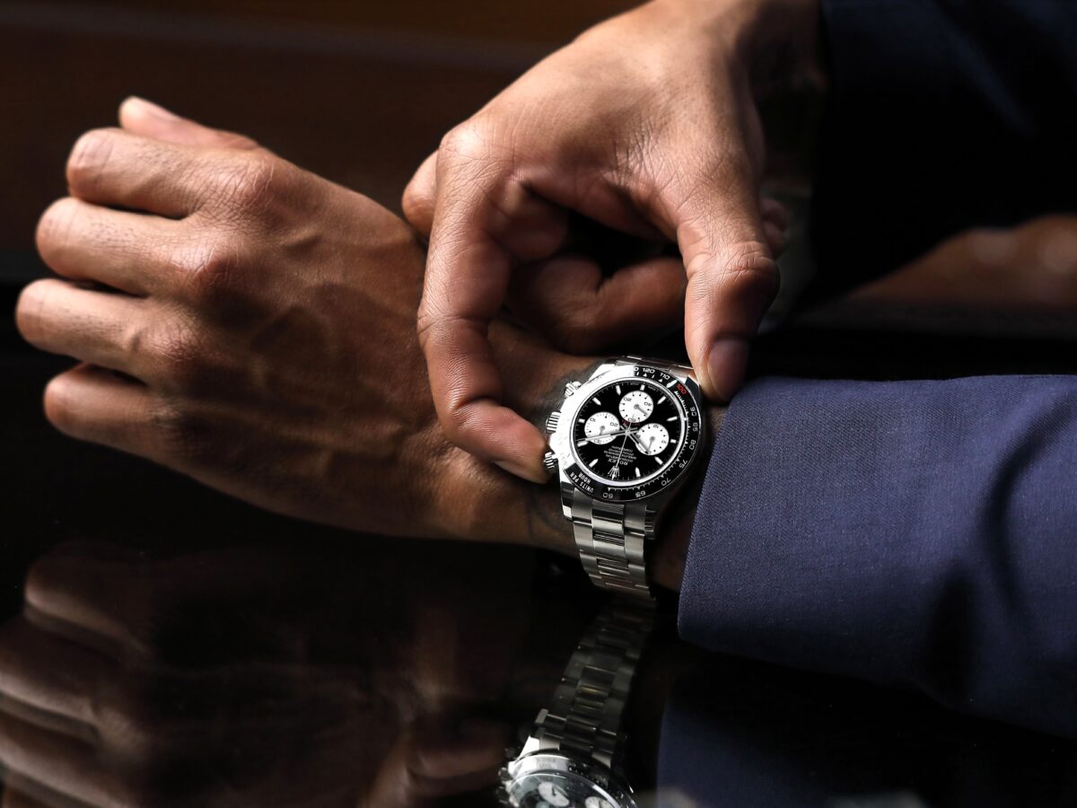 Close-up of a man adjusting a black dial Rolex Cosmograph Daytona on his wrist to demonstrate proper fit.