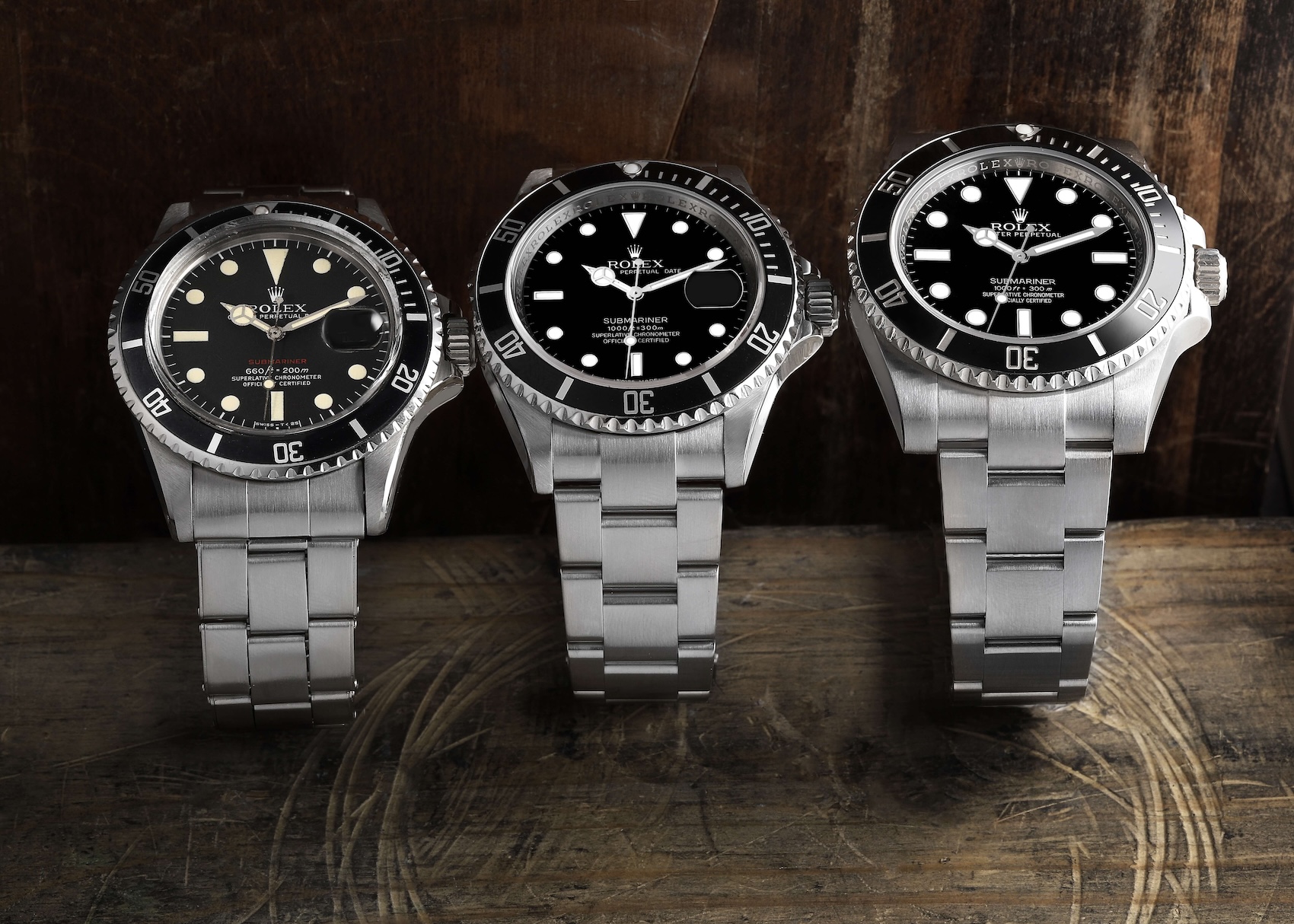 Three generations of Rolex Submariner watches side-by-side, showcasing the evolution of the Oyster case over decades.