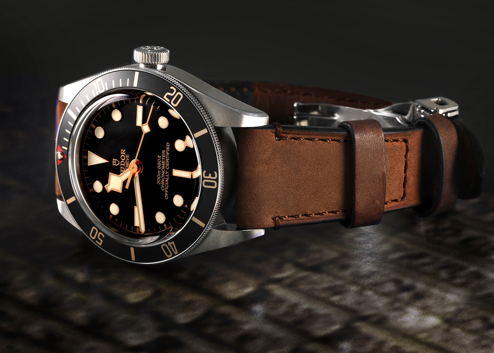 A Tudor Black Bay Fifty-Eight 39mm with a black dial and gilt accents, shown on a brown leather strap against a dark, textured background.