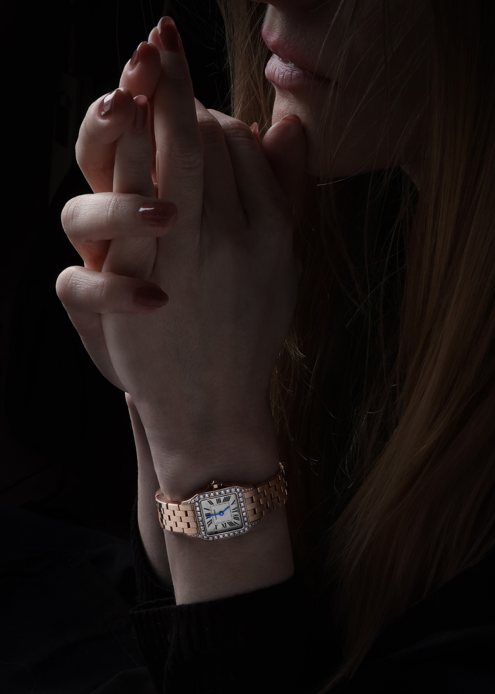 Woman's hands clasped wearing a rose gold Cartier Santos Demoiselle watch with a diamond bezel.