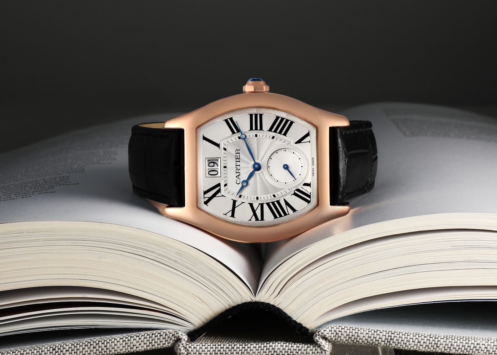 Rose gold Cartier Tortue XL watch with a silver guilloche dial resting on an open book.