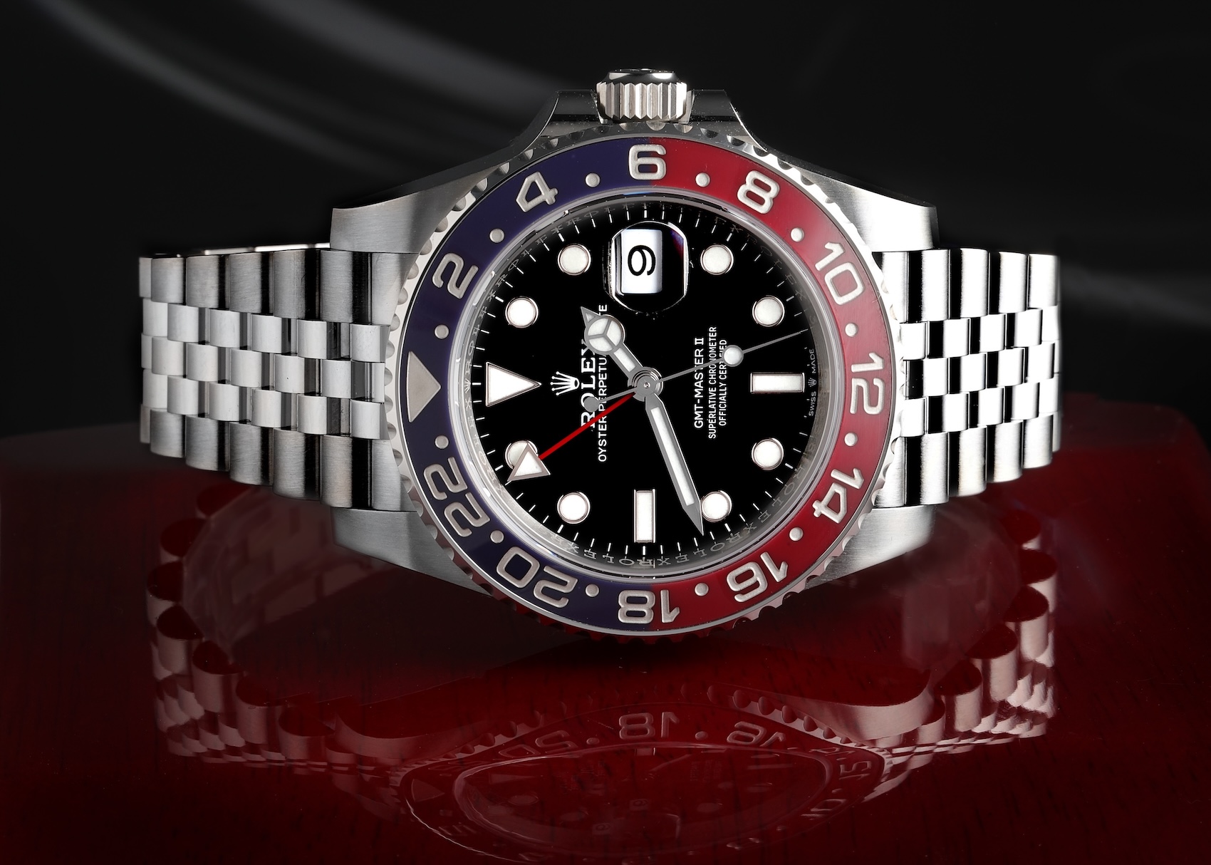 A close-up front view of the modern stainless steel Rolex GMT-Master II Pepsi (Ref. 126710BLRO) featuring the bi-color blue and red ceramic bezel and a Jubilee bracelet, resting on a reflective wooden surface.