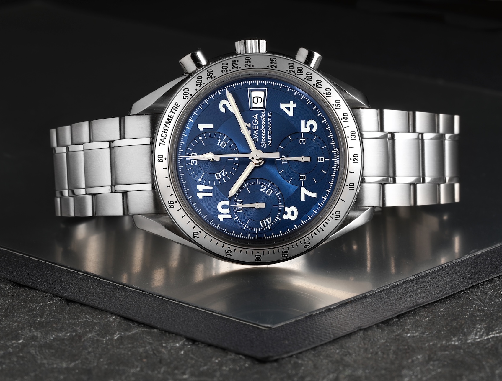 Omega Speedmaster Date 39mm with blue dial resting on a dark slate surface