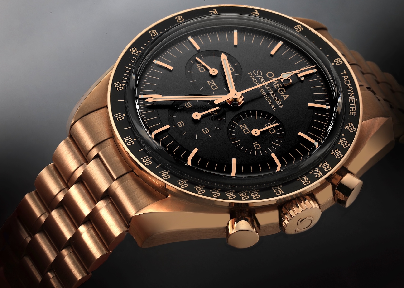 A macro close-up of an Omega Speedmaster Professional watch in solid 18K Sedna Gold. It features a deep black dial with rose gold hands and hour markers, and is attached to a matching solid Sedna Gold bracelet. The focus is sharp on the case and subdials.