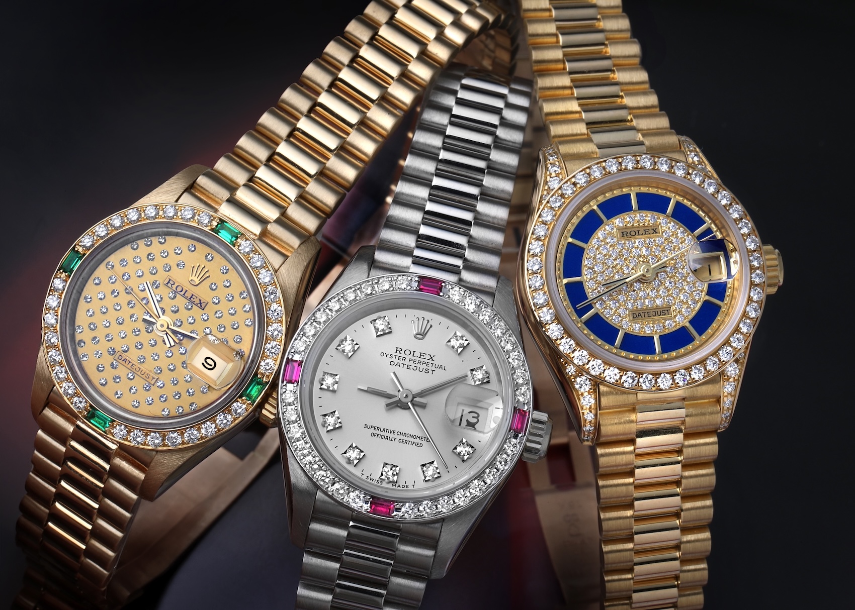 Group of three gem-set ladies Rolex Datejust President watches in yellow gold and white gold featuring diamonds, emeralds, rubies, and lapis lazuli.