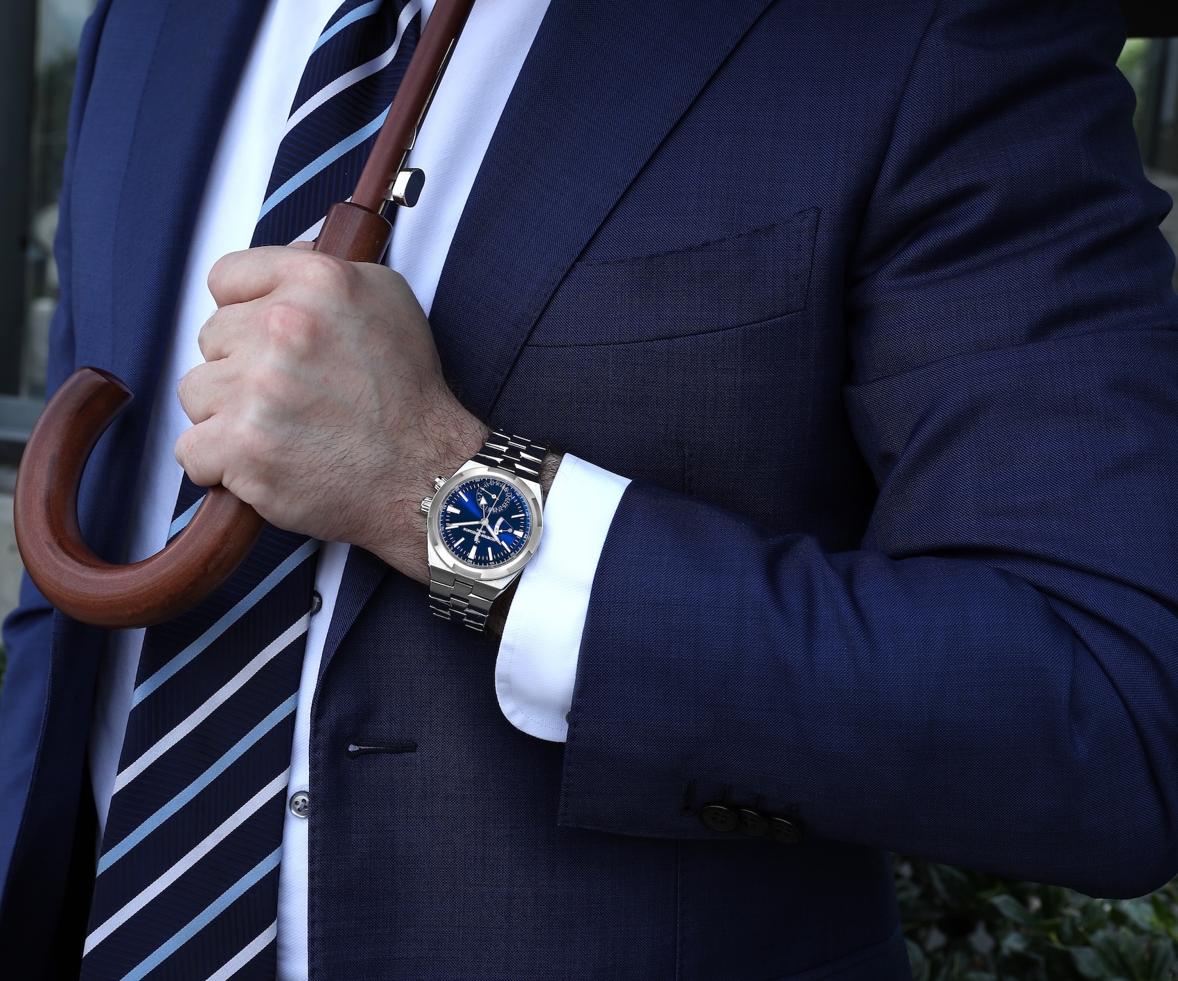 A man wearing a Vacheron Constantin Overseas Dual Time watch with a blue dial in a professional lifestyle setting.