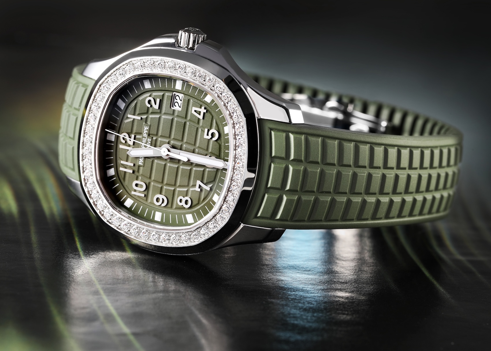 A detailed product shot of the Patek Philippe Aquanaut Luce Ref. 5267/200A resting on a surface. The focus is on the integrated dark green composite strap, which features a textured pattern that complements the dial. The stainless steel deployant clasp and diamond bezel are visible.