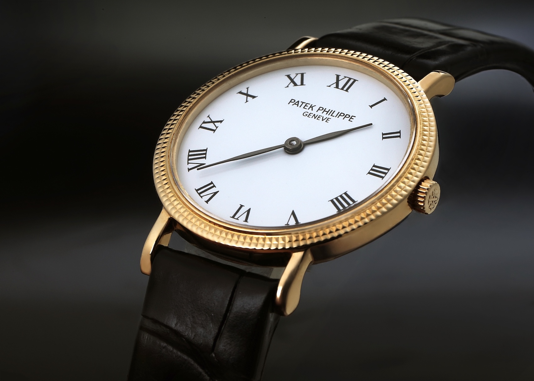 An angled close-up of the Patek Philippe Calatrava Ref. 4819J in 18k yellow gold. The watch features a pristine white dial with black Roman numerals, elegant black hands, and the signature Clous de Paris hobnail bezel, paired with a classic black leather strap.