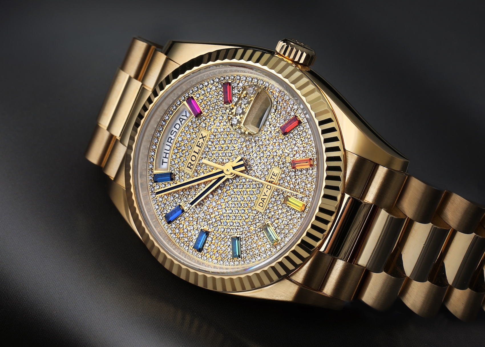 Rolex Day-Date 36 in yellow gold with a spectrum of rainbow sapphire baguette markers on a pave diamond dial.