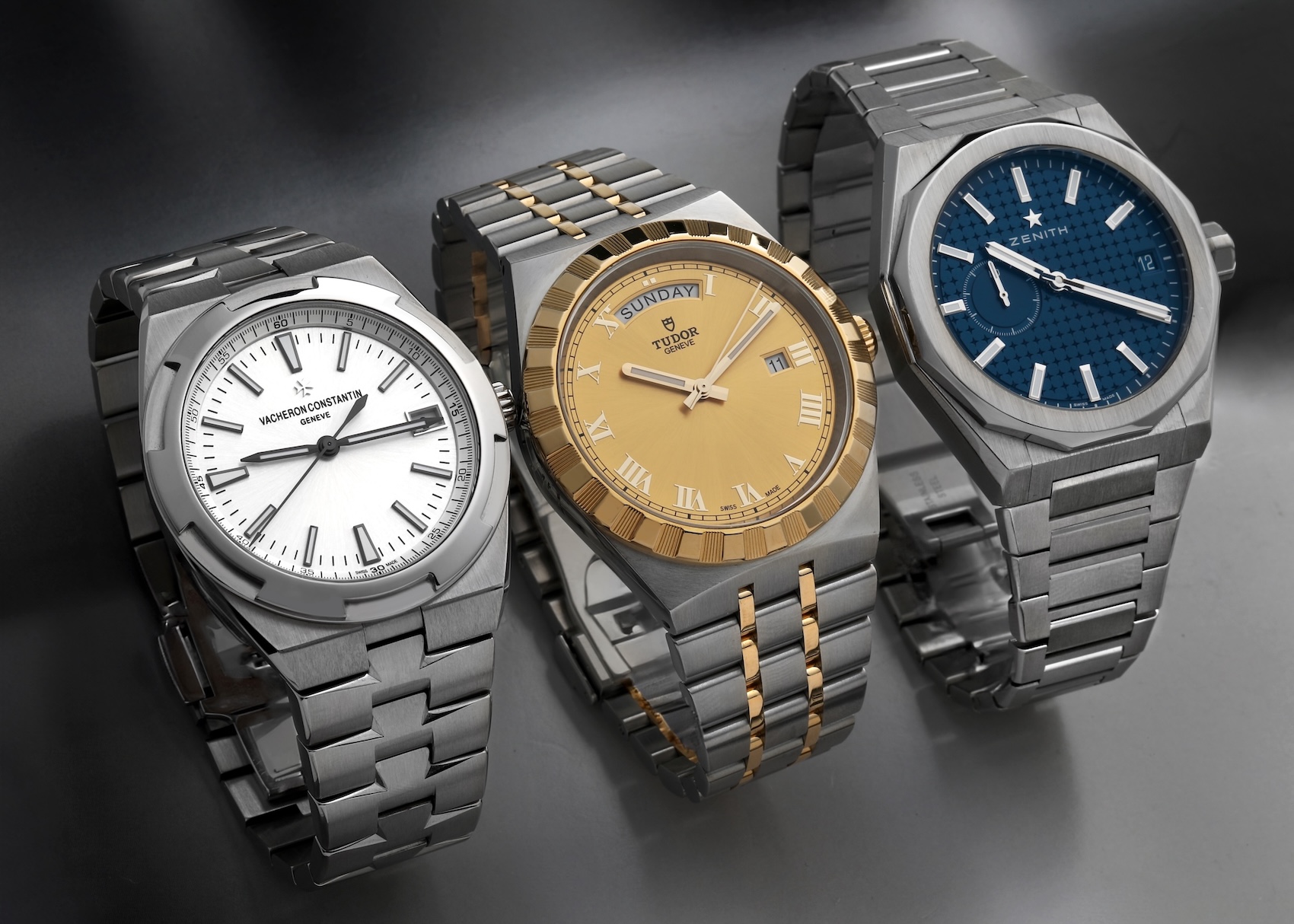 Three luxury watches with integrated bracelets (Vacheron Constantin Overseas steel, Tudor Royal two-tone, Zenith Defy Skyline steel) displayed together in a row.