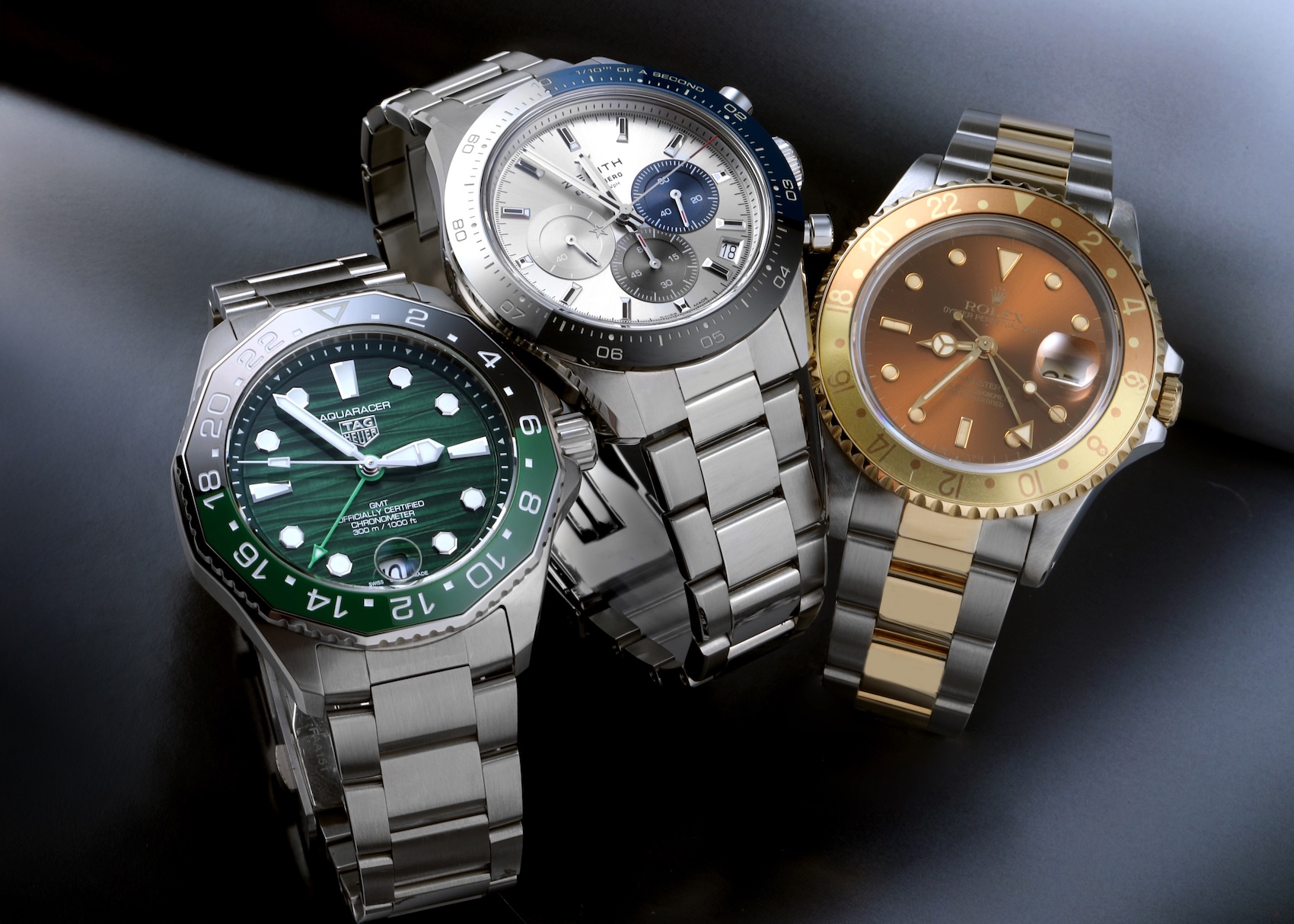 Group of three luxury men's watches featuring a green TAG Heuer Aquaracer, silver Zenith Chronomaster Sport, and two-tone Rolex GMT-Master II Root Beer.
