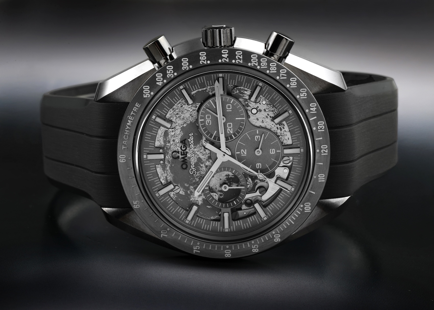 Straight-on view of the Omega Speedmaster Grey Side of the Moon watch, showcasing the laser-ablated lunar dial, black ceramic bezel, and integrated grey rubber strap.