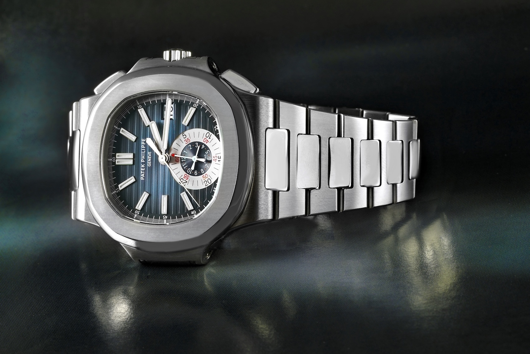 View of a Patek Philippe Nautilus Chronograph Ref 5980 in steel showing the iconic porthole case shape, blue horizontally embossed dial, and integrated bracelet.