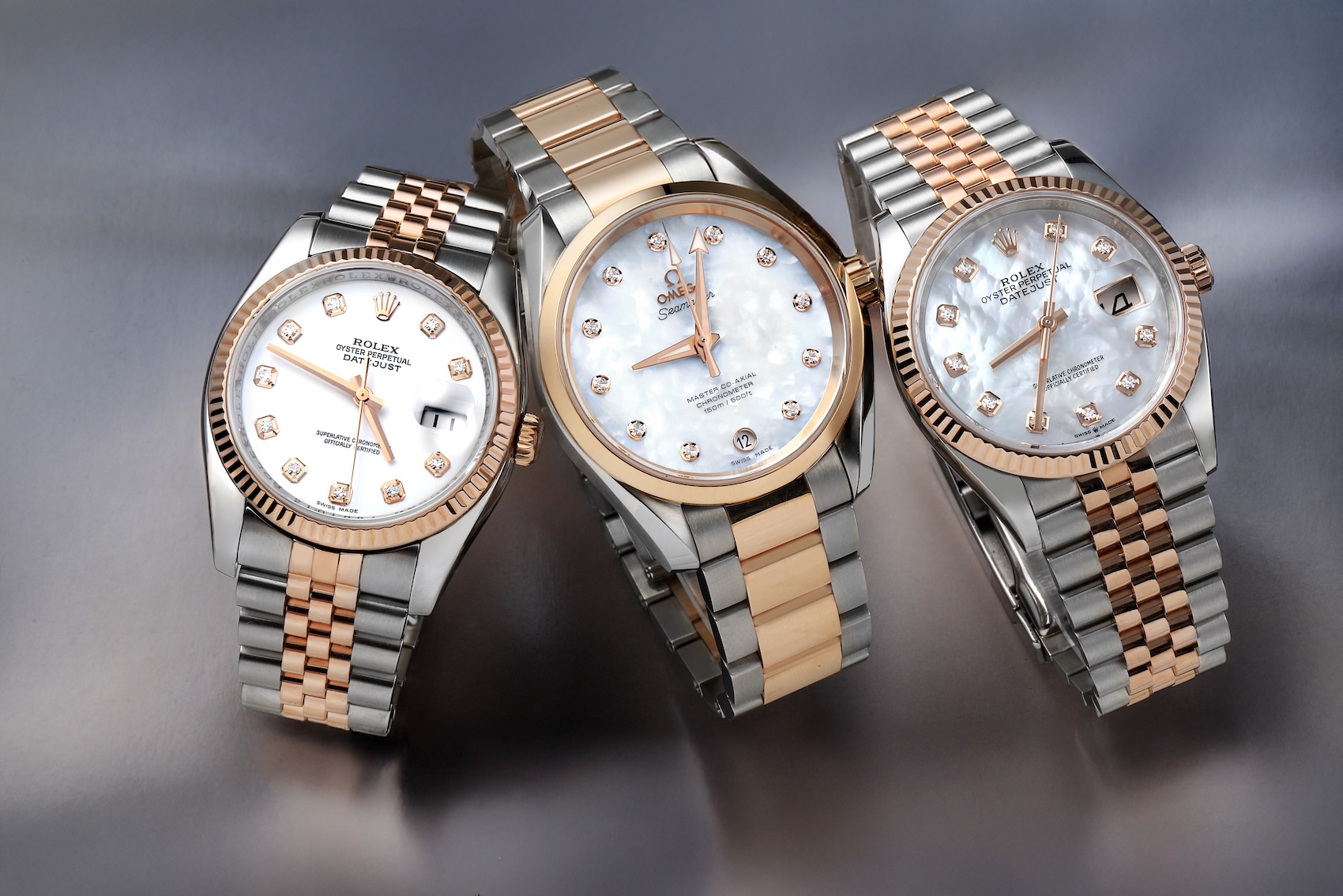 A group shot featuring two Rolex Datejust watches and one Omega Aqua Terra, all in two-tone rose gold and steel with mother-of-pearl dials and diamond hour markers.
