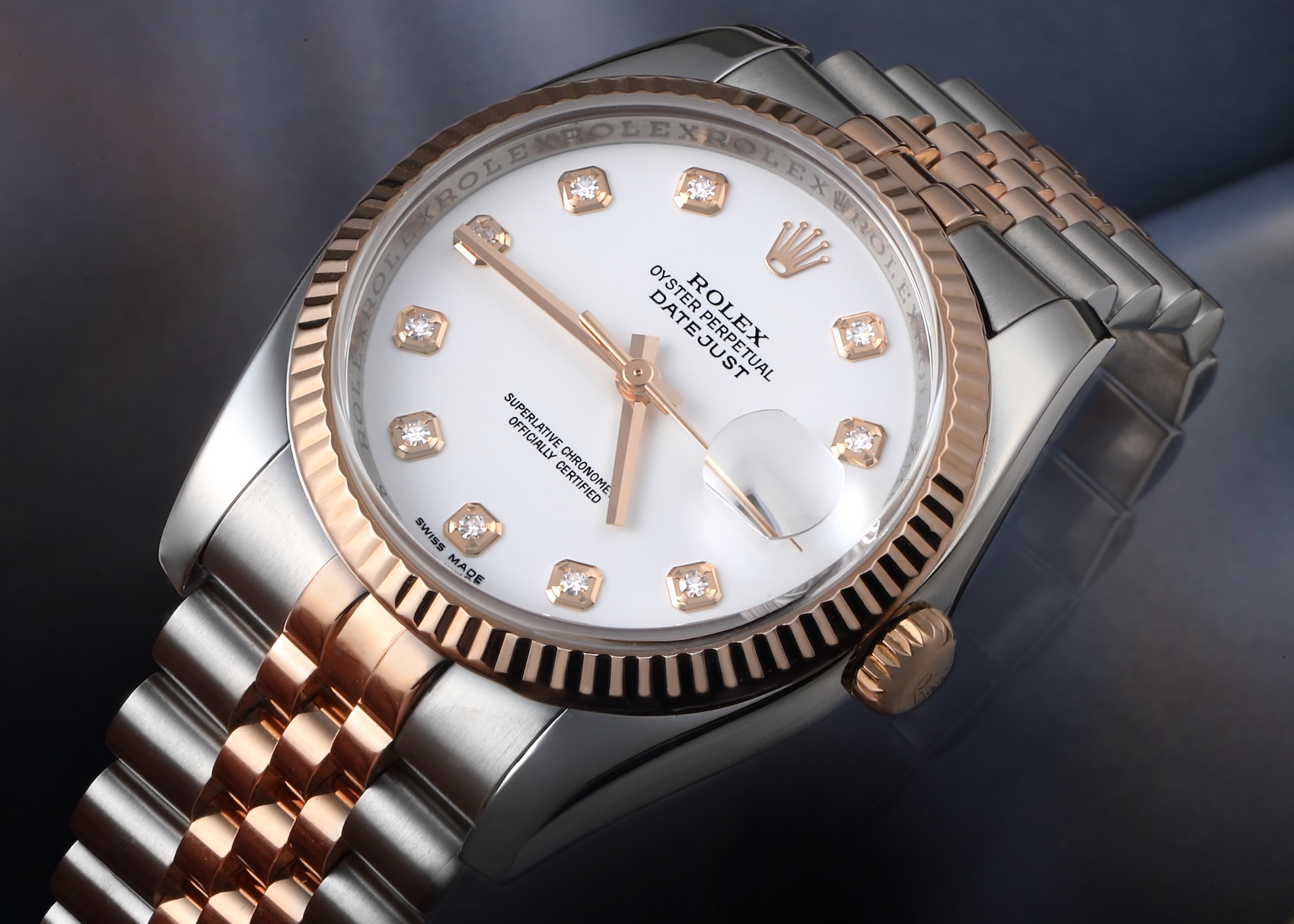 Macro shot of a Rolex Datejust in two-tone rose gold and stainless steel, featuring a white dial, diamond hour markers, and a fluted bezel.